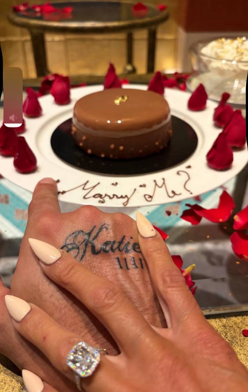 In a moment dripping with sentiment, Price placed her hand tenderly over her fiancé's, showing off both her massive diamond sparkler and his "Katie" tattoo, next to a decadent rose-petal-strewn dessert that read "Marry Me?" | Source: Instagram/katieprice
