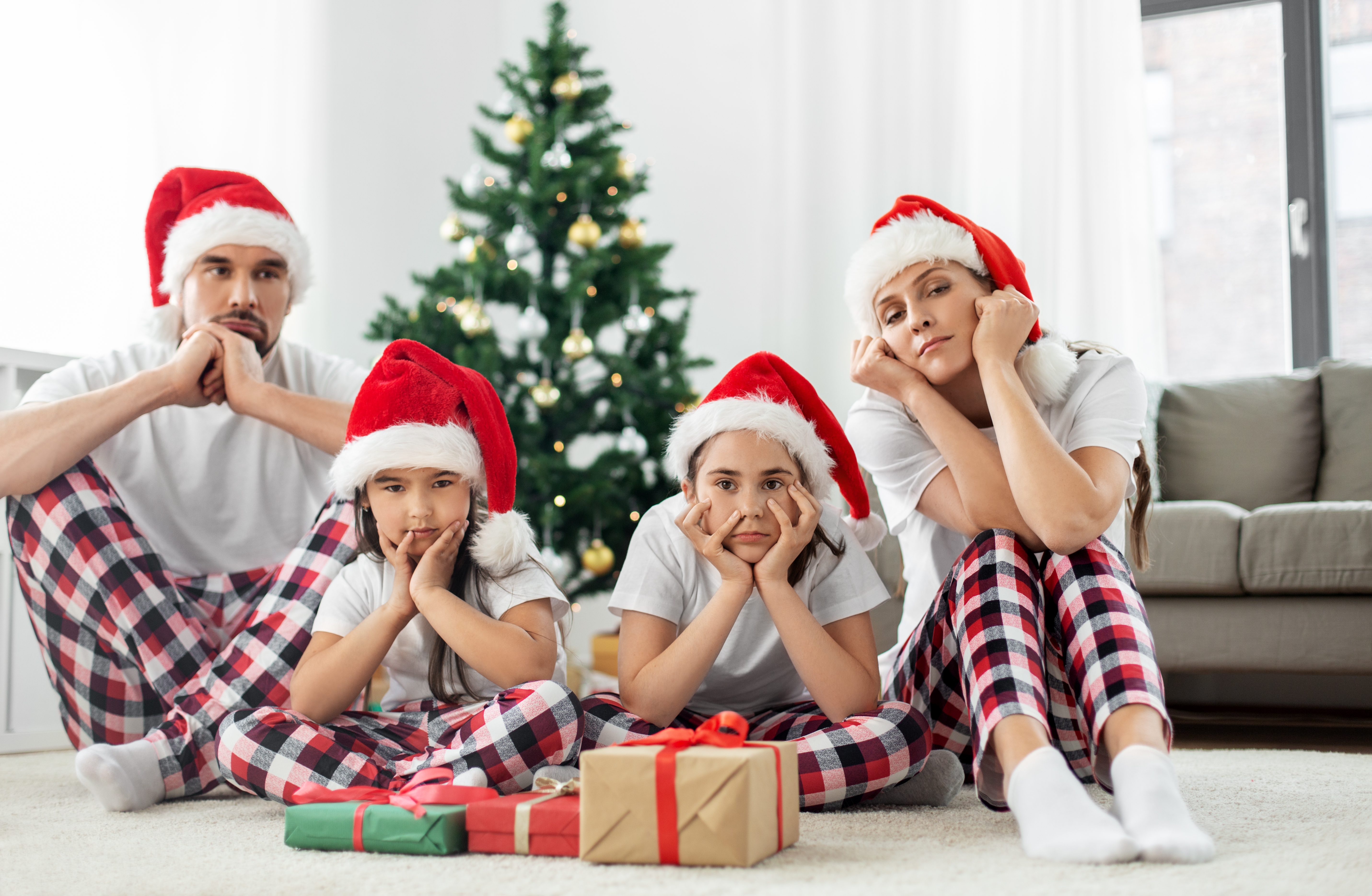 A depressed family of four sitting near a Christmas tree wearing Santa caps | Source: Shutterstock