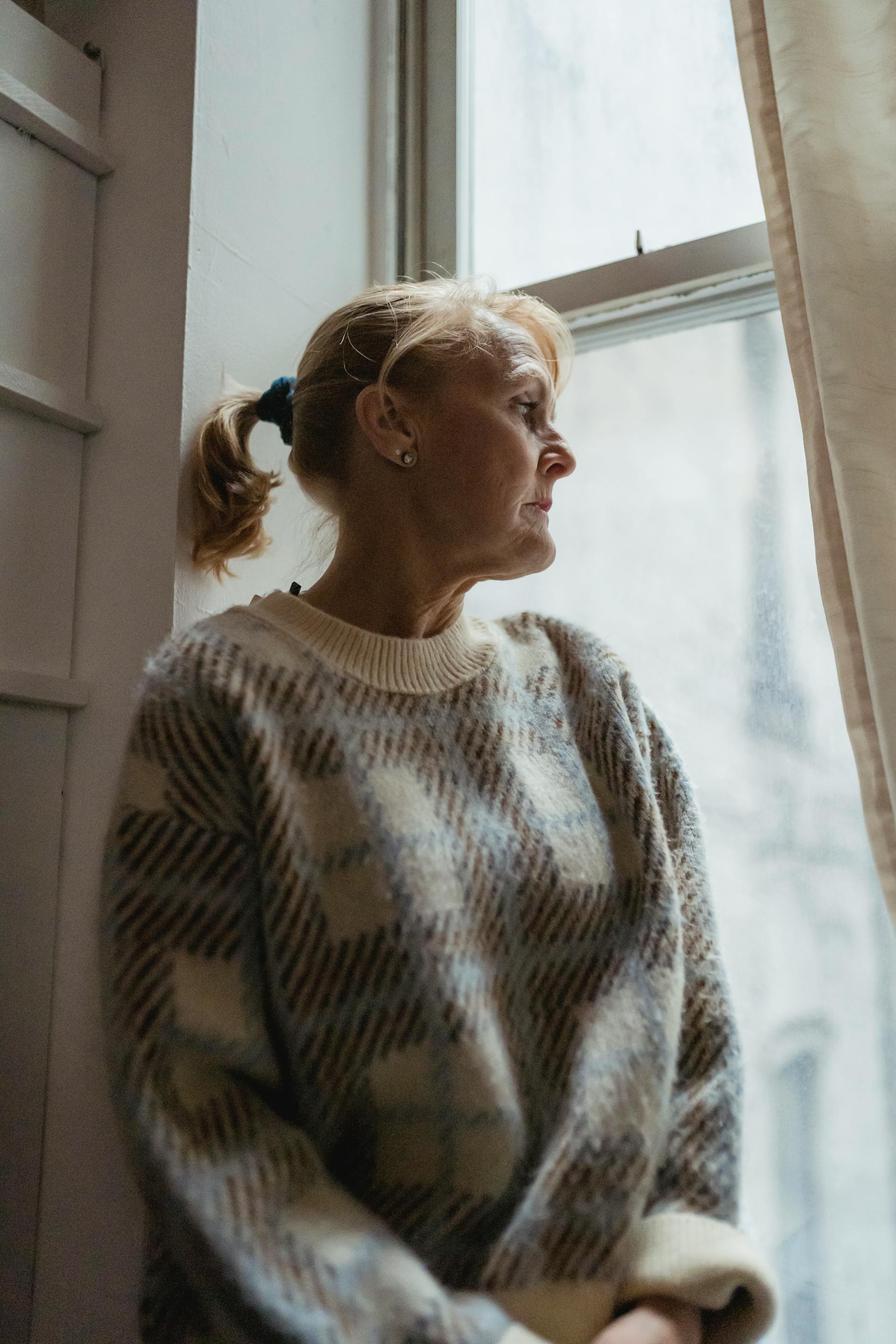 A wistful middle-aged woman looking out the window | Source: Midjourney