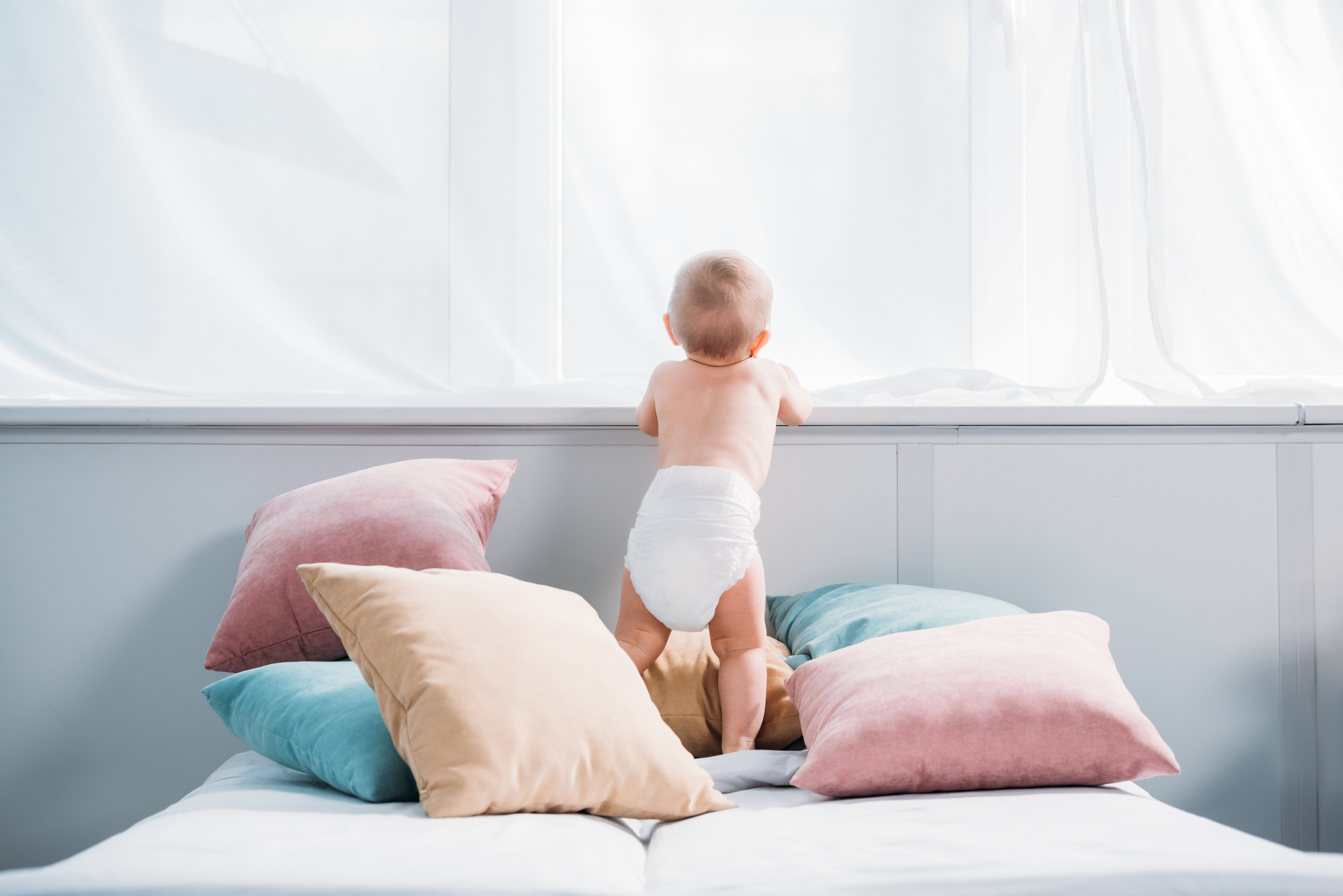 Baby in diaper standing on bed. | Photo: Shutterstock
