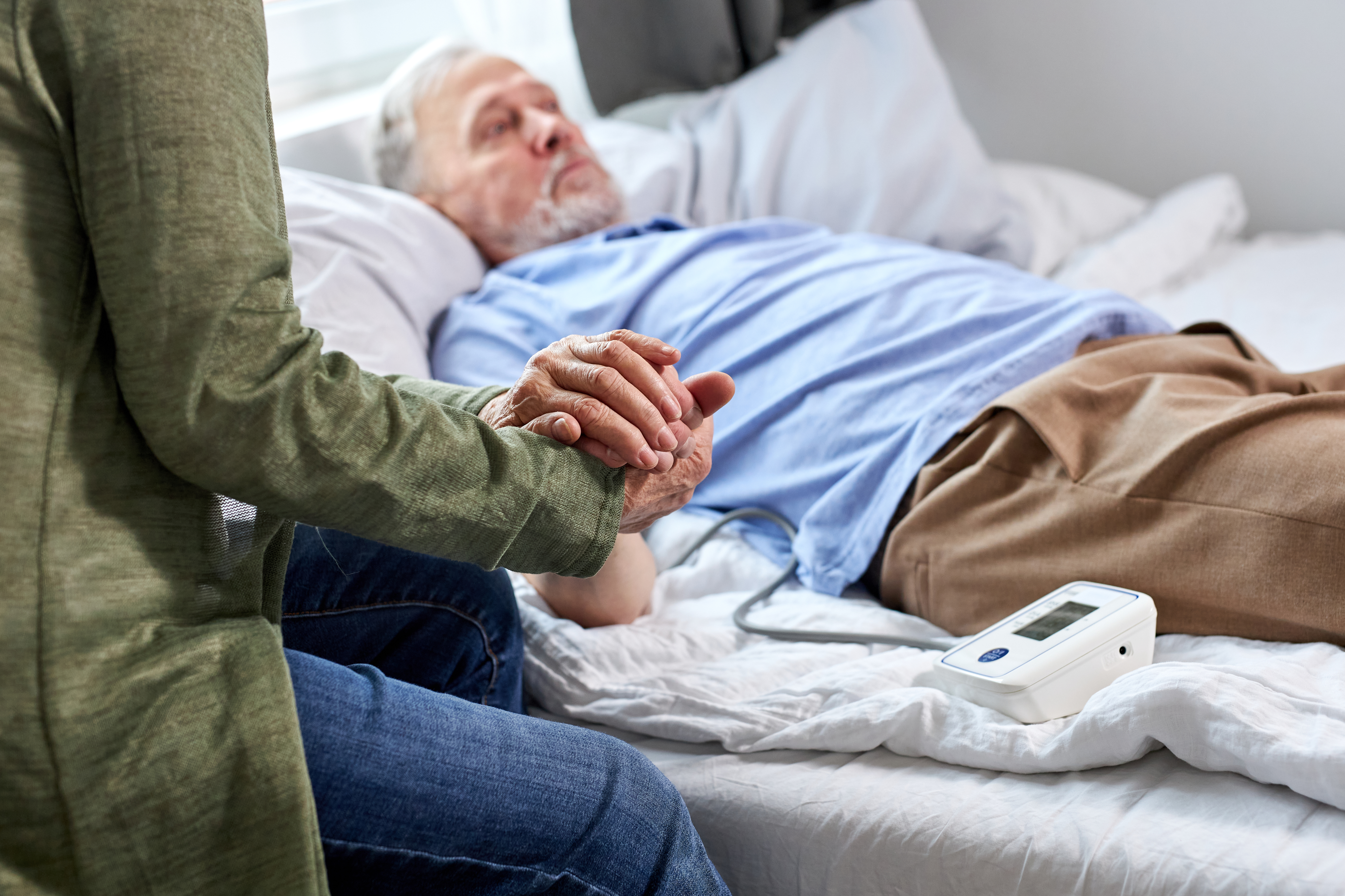 A woman holding an ailing elderly man's hand while sitting beside him | Source: Shutterstock