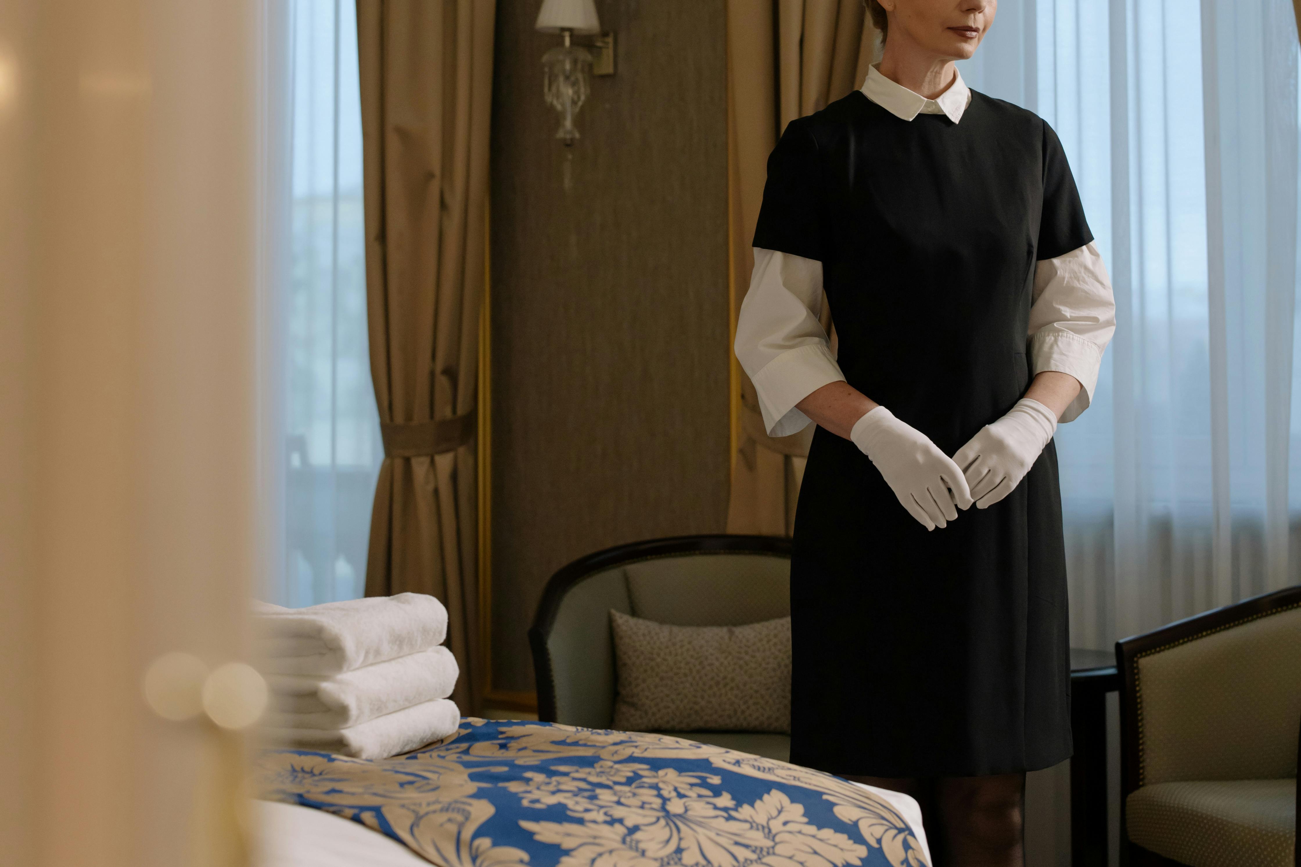 Mujer de uniforme junto a la cama de la habitación del hotel | Fuente: Pexels