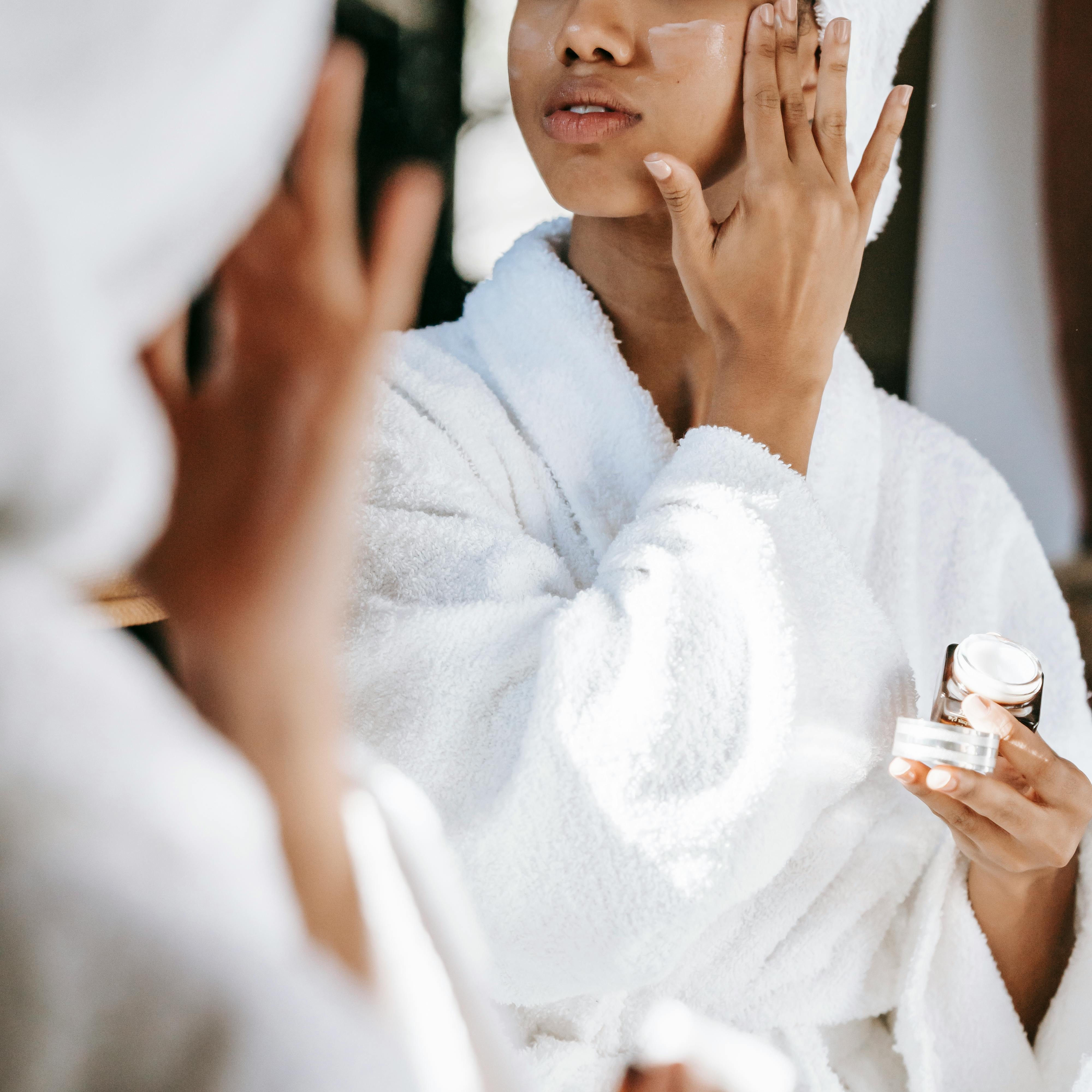 A woman in a dressing gown, applying moisturizing lotion | Source: Pexels