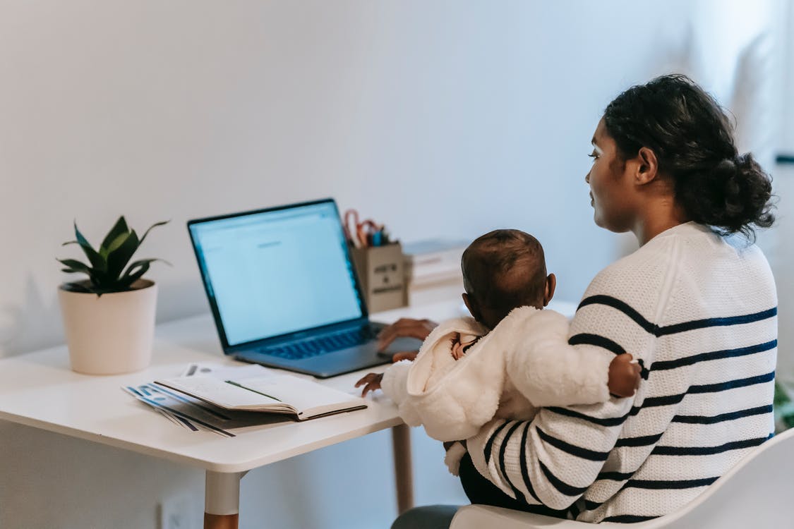 Madre trabajando frente al ordenador con su bebé en brazos. | Foto: Pexels