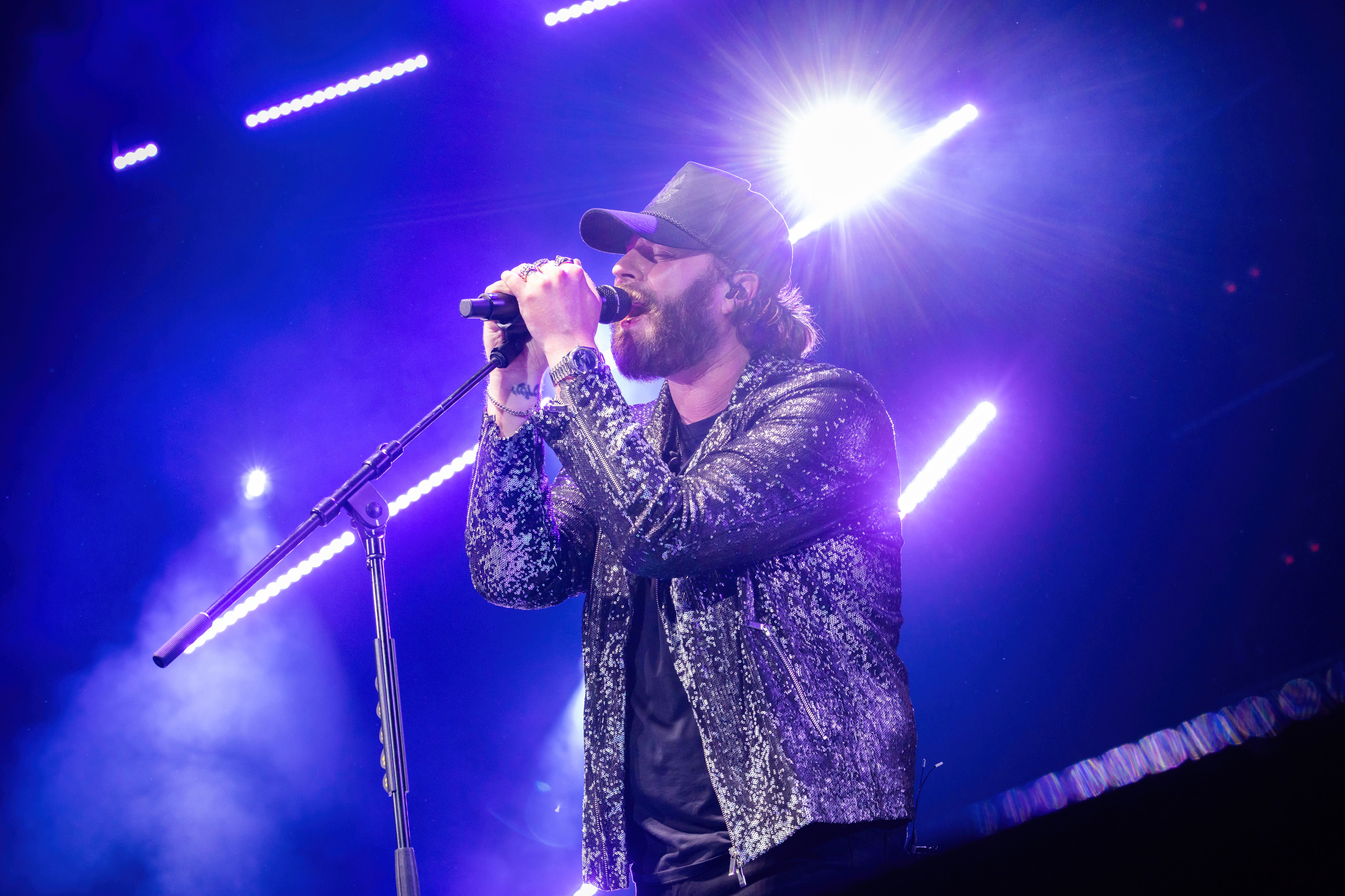 Nate Smith grips the microphone with both hands and leans into an impassioned performance, his sparkling jacket gleaming beneath brilliant blue and purple lights.