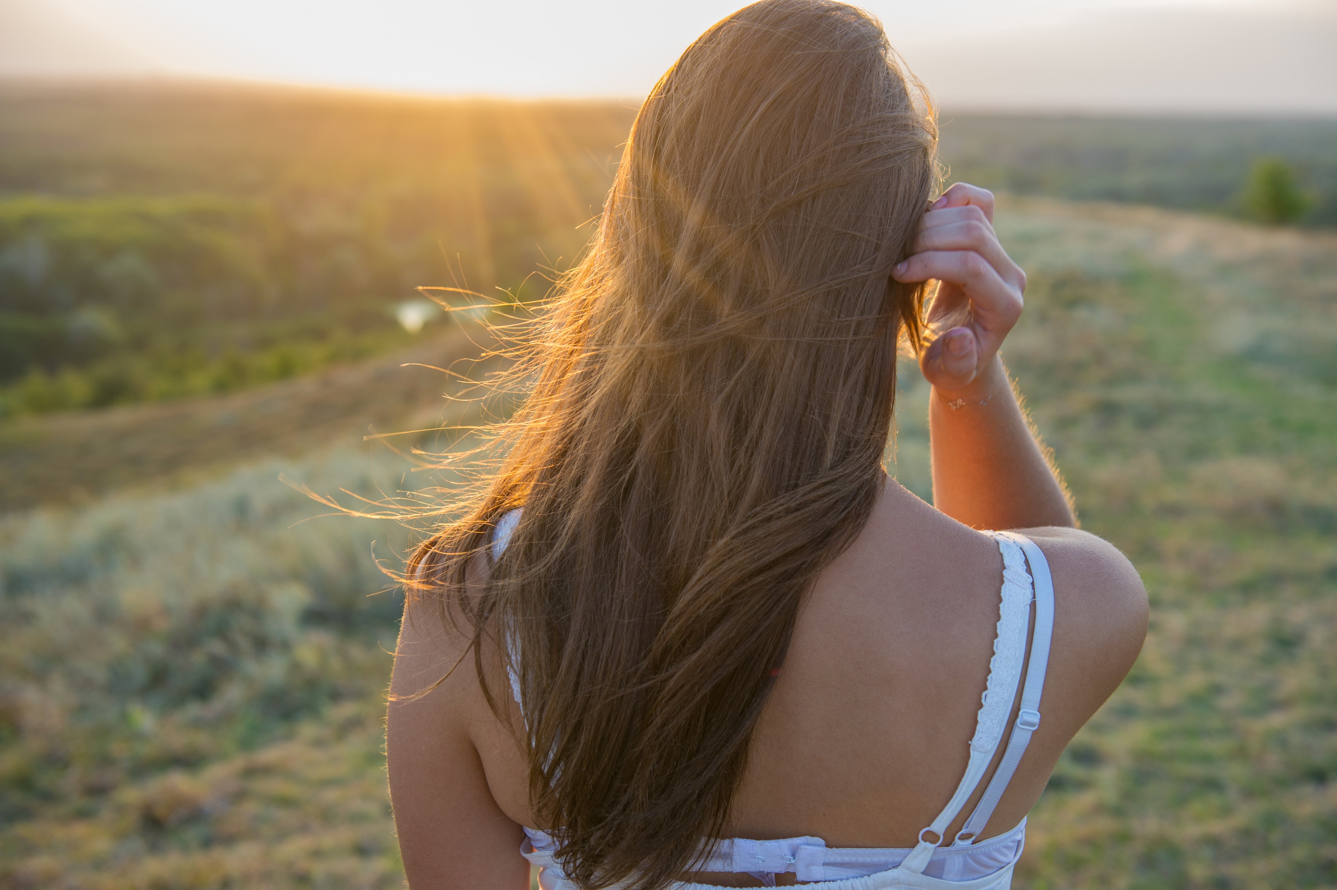 Une fille de dos au coucher du soleil dans la prairie. | Photo : shutterstock