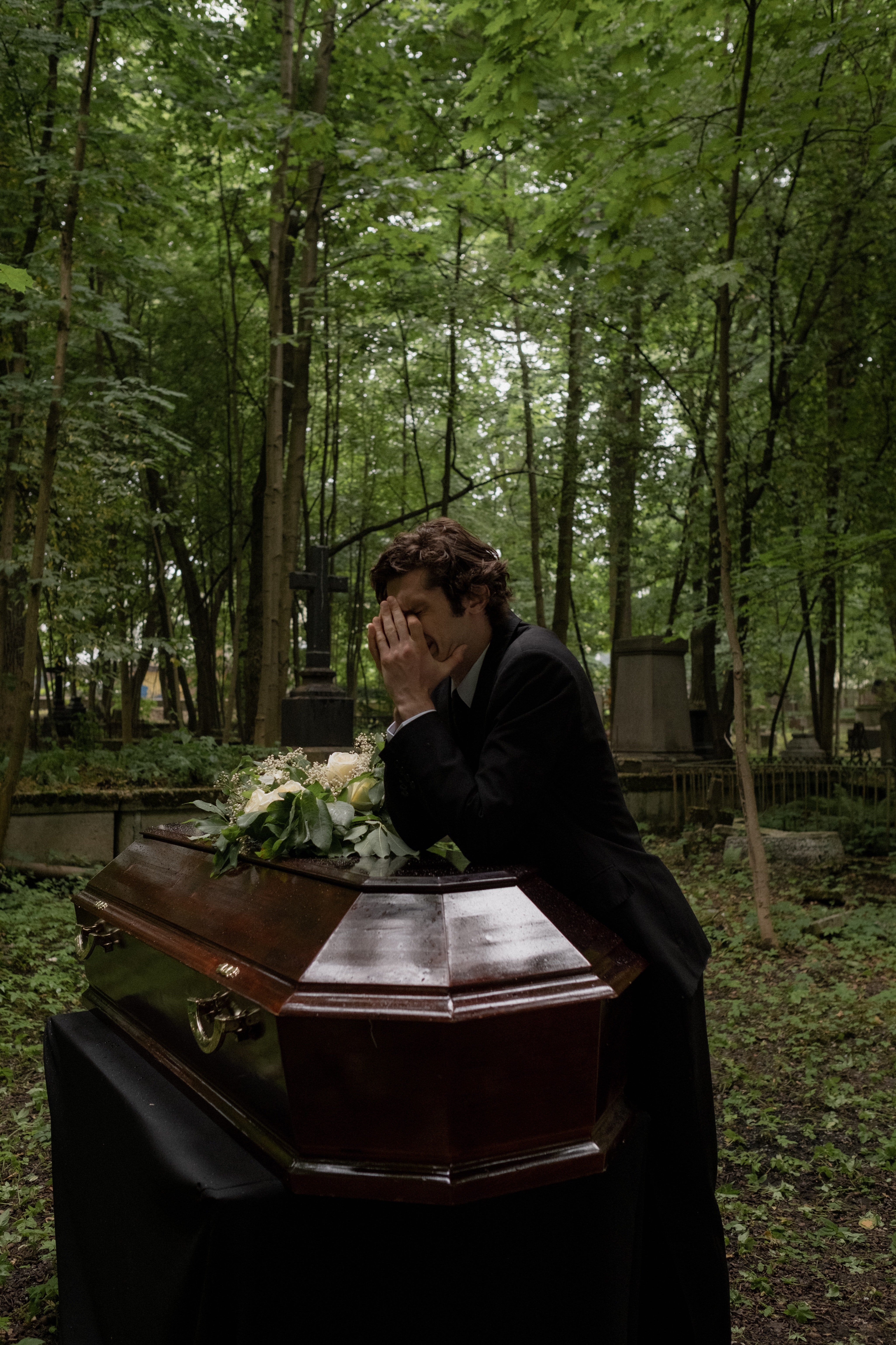 A despondent man pictured resting his arms on the coffin. | Source: Pexels