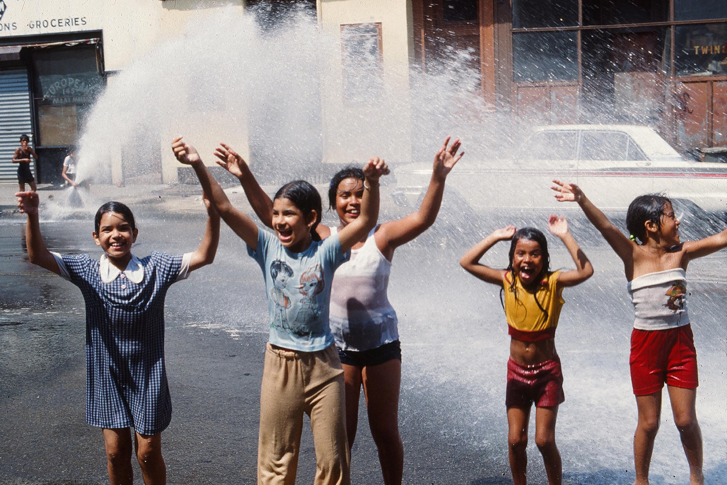 On an unidentified Brooklyn street, a group of young girls play in the water from an opened fire hydrant in the wake of the New York City blackout on July 14, 1977. | Source: Getty Images