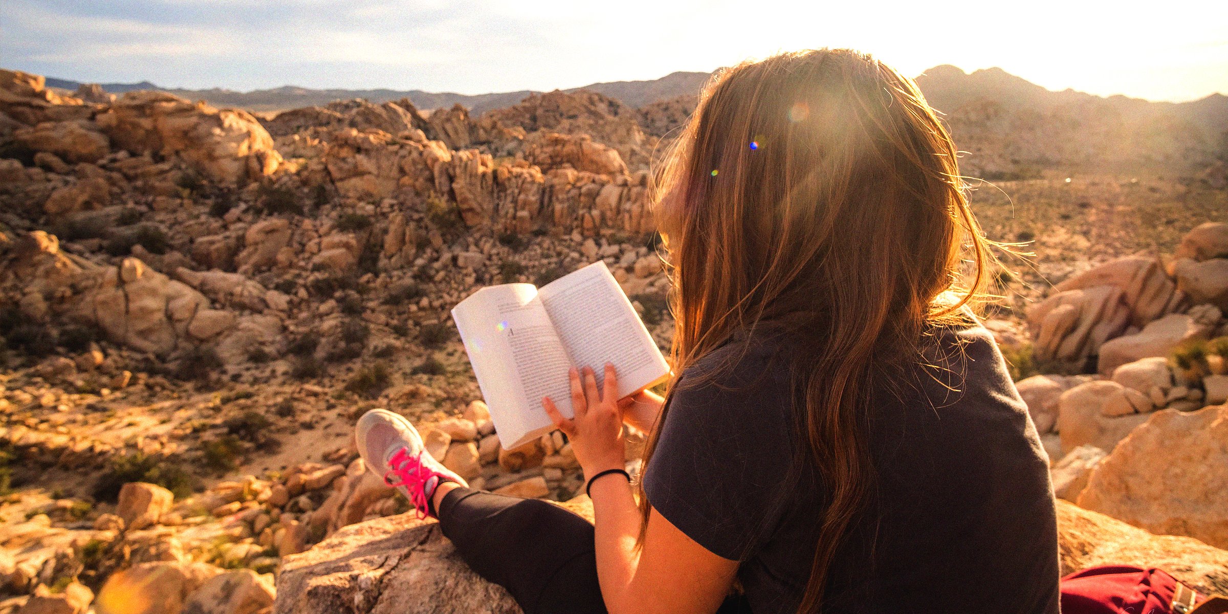 Unsplash | A woman reading a book while in a rocky terrain