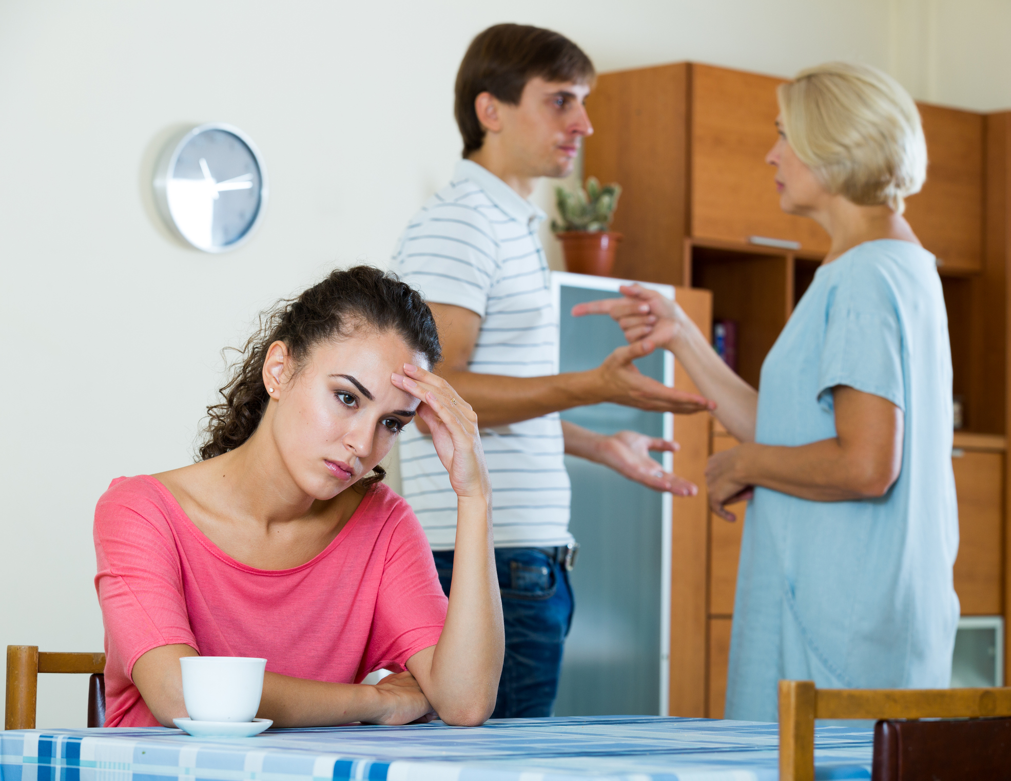 An annoyed woman sitting in the foreground while an older one and a younger man argue | Source: Getty Images