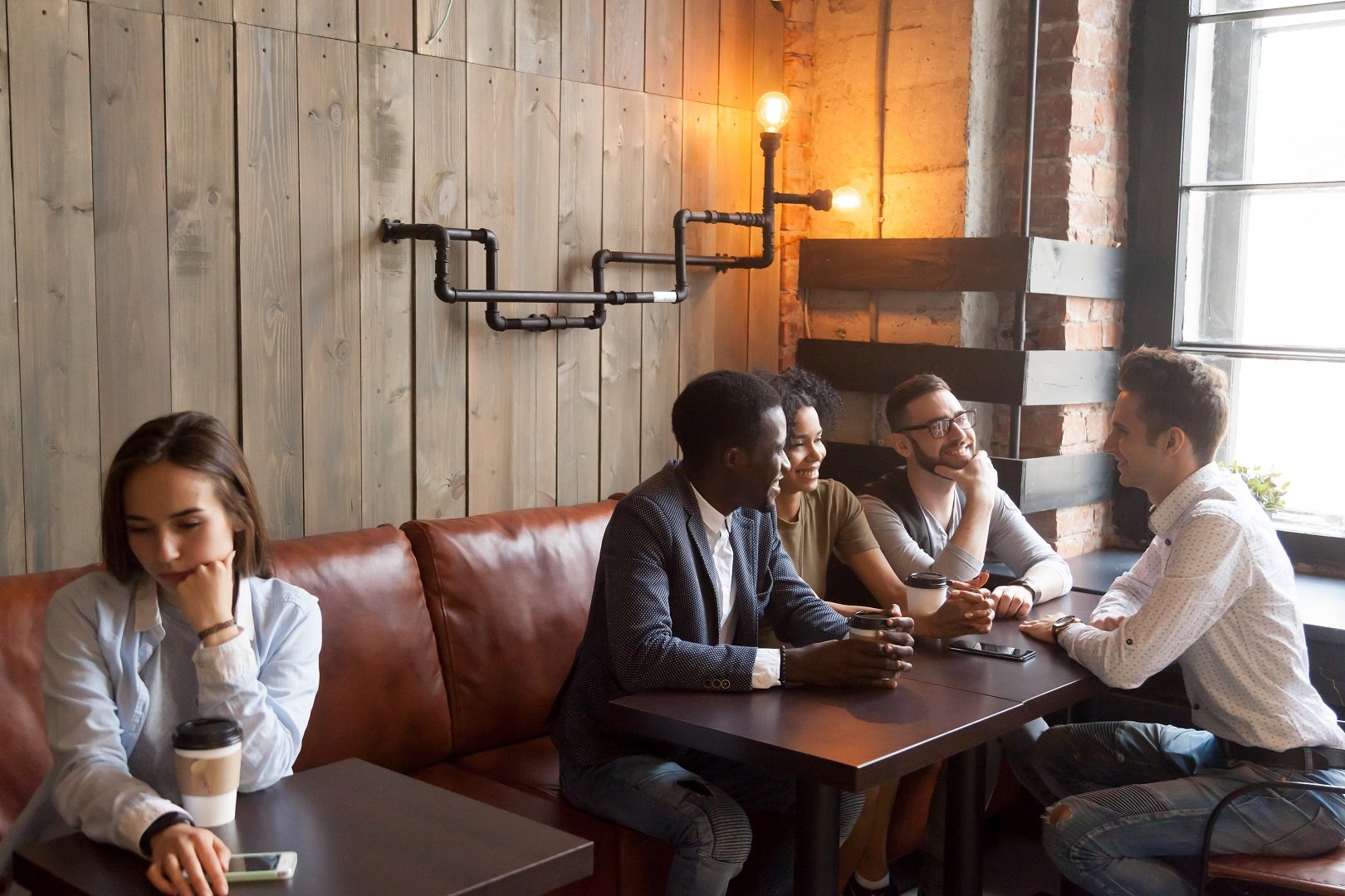 Joven mujer sentada junto a reunión de amigos || Fuente: Shutterstock Joven mujer sentada junto a reunión de amigos || Fuente: Shutterstock