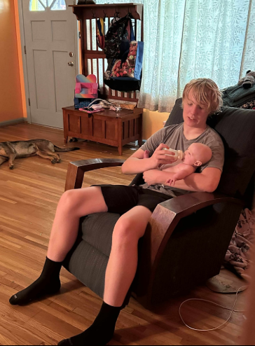 Caleb Moore sitting on a chair while feeding a baby, dated June 13, 2025 | Source: Gofundme