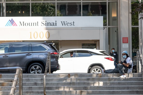 A man wearing a mask sits on the steps outside Mount Sinai West Hospital. | Photo: Getty Images