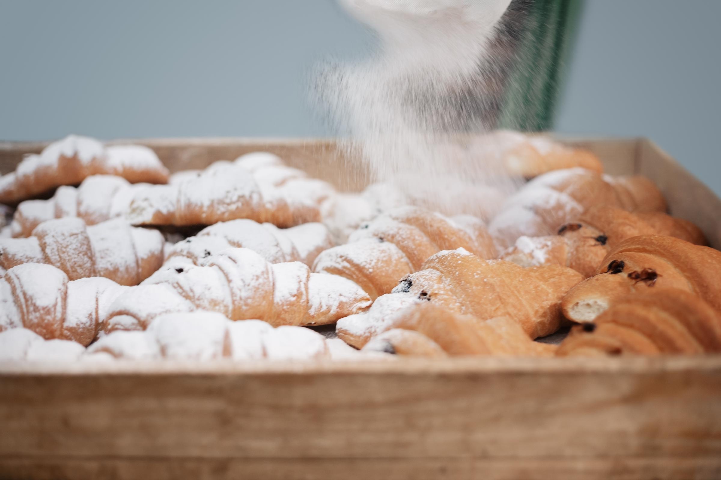 Powdered sugar falling onto a wooden tray full of freshly baked croissants | Source: Getty Images