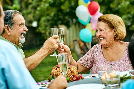 Photo of happy senior couple toasting champagne flutes while sitting at dining table. | Photo: Getty Images