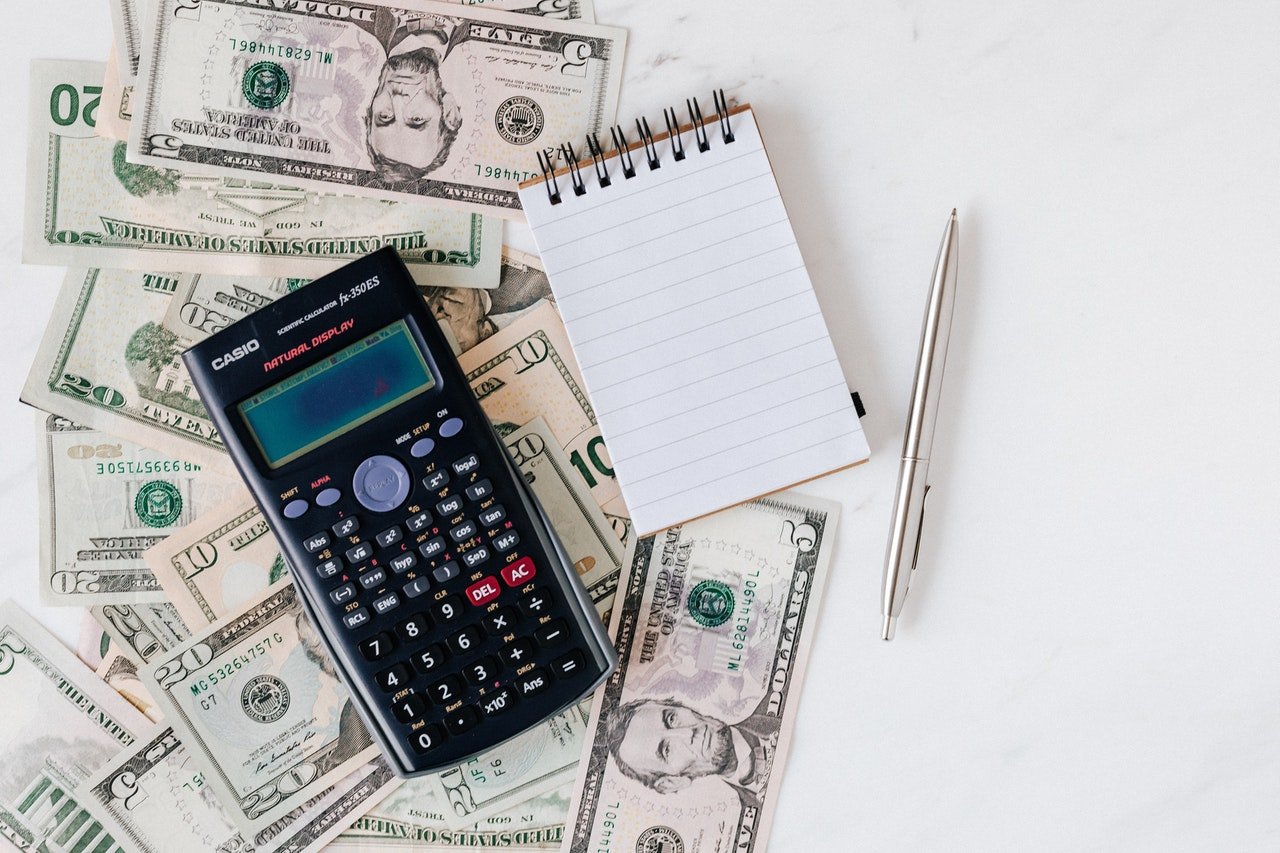 Calculator and notepad over U.S. dollar notes | Source: Pexels