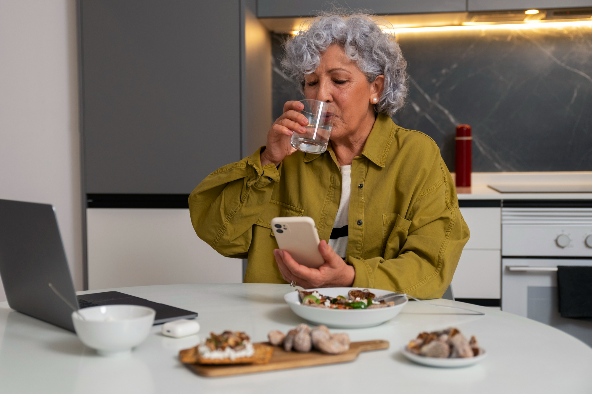 A woman sitting in the kitchen enjoying a meal and looking at her phone. For illustration purposes only | Source: Freepik