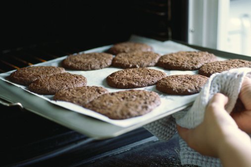  woman taking sheet of baked cookies out of the oven | Photo: Getty Images