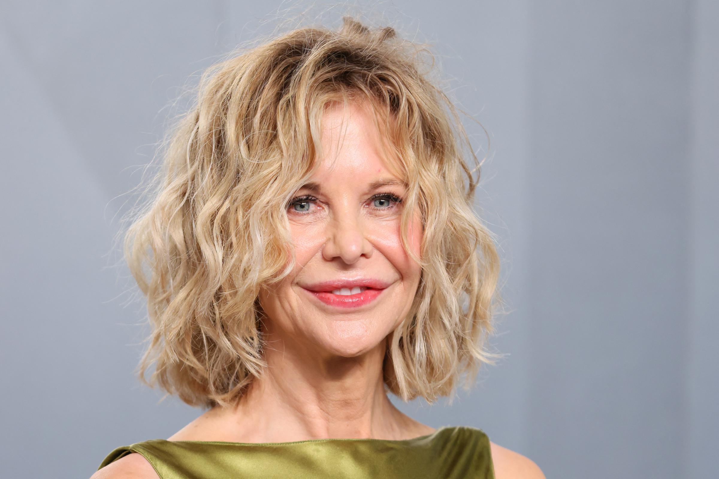 Meg Ryan smiles toward photographers at the Vanity Fair Oscar Party, showcasing the luminous sheen of her olive satin gown and a polished look that blends classic elegance with modern style.