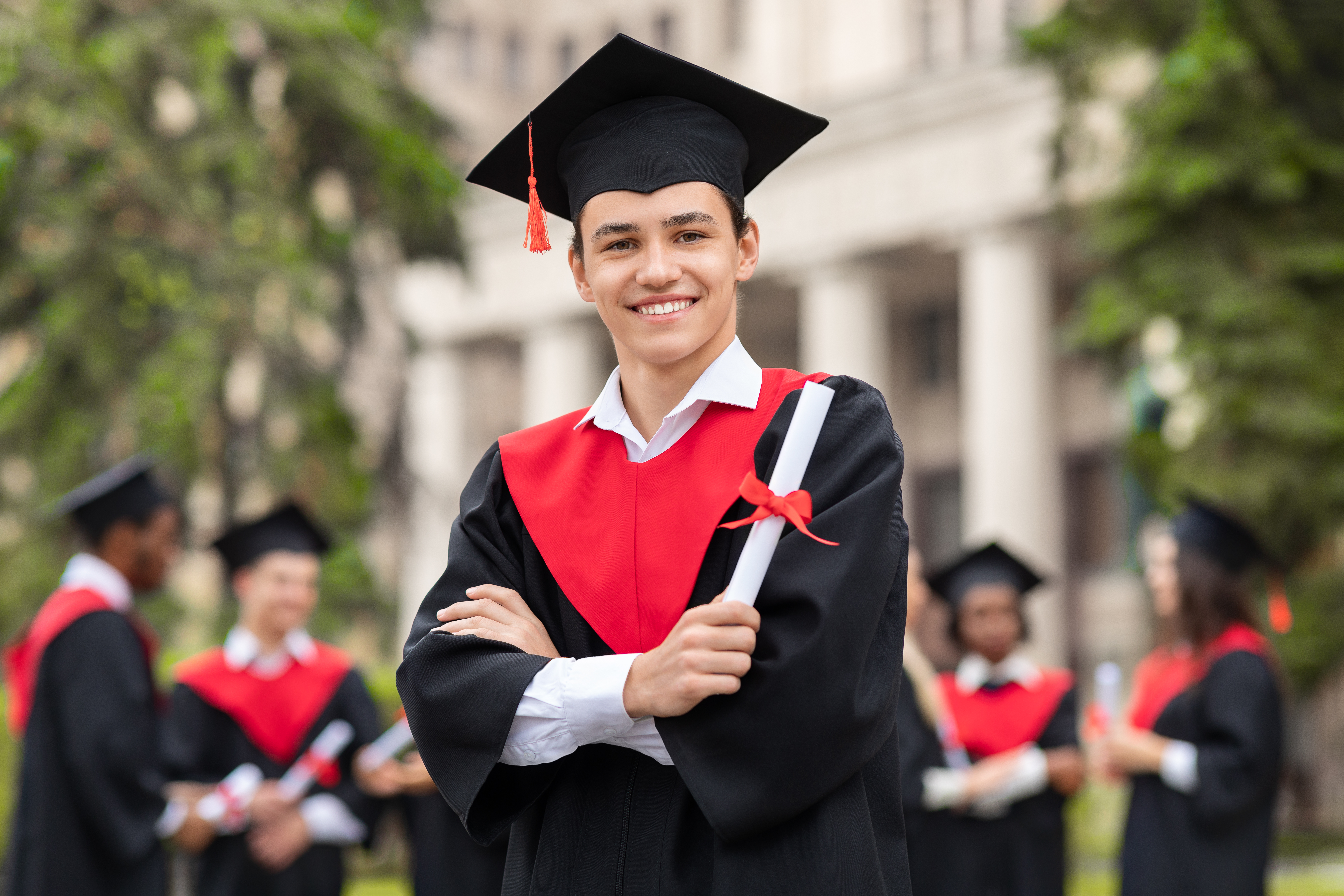 Cheerful guy in graduation costume showing his diploma and smiling at camera. | Source: Shutterstock