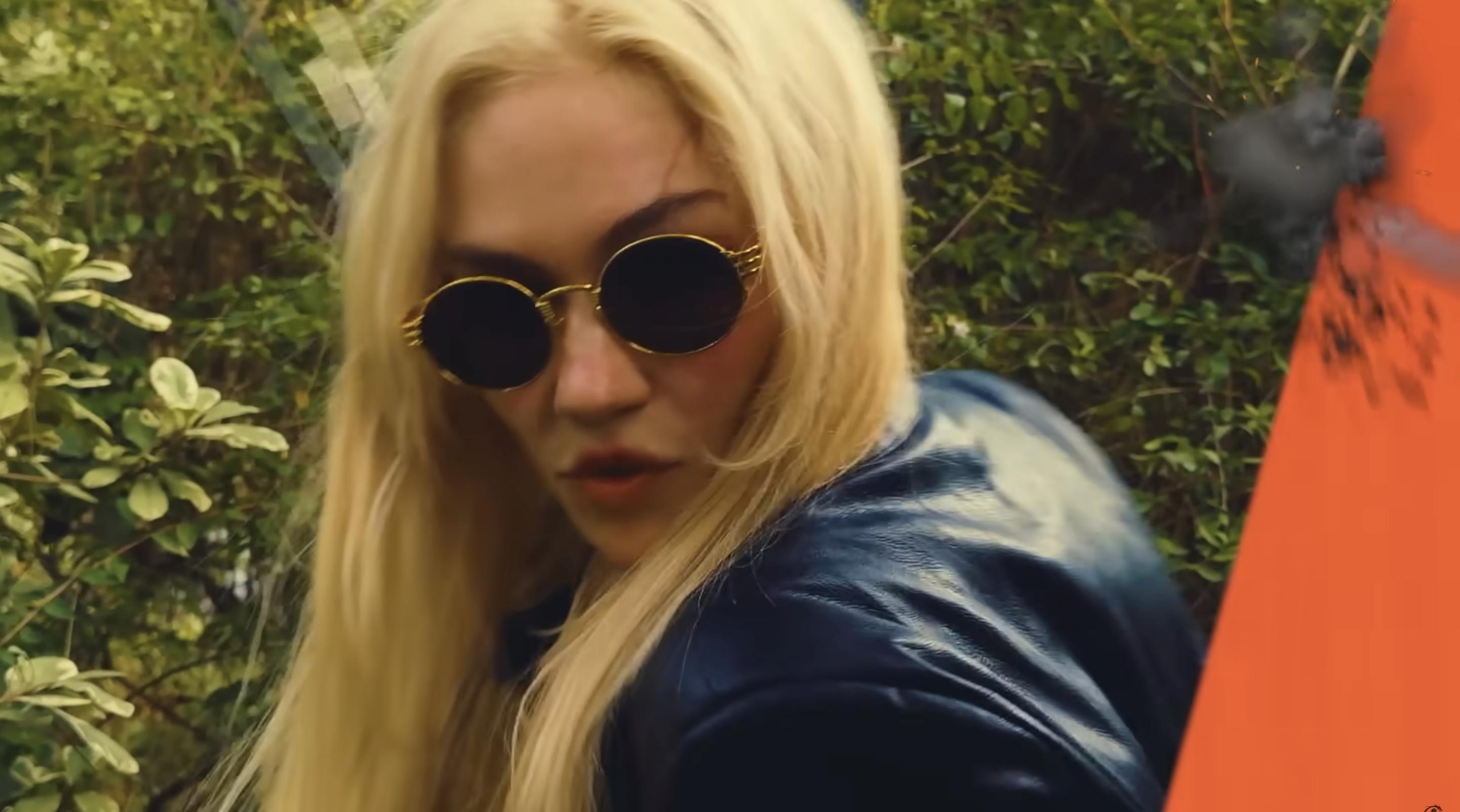 Grimes is seen in a forest wearing sunglasses and a black leather jacket, with faint tattoo lines just visible under her hair, as posted on October 21, 2025 | Source: YouTube/grimes