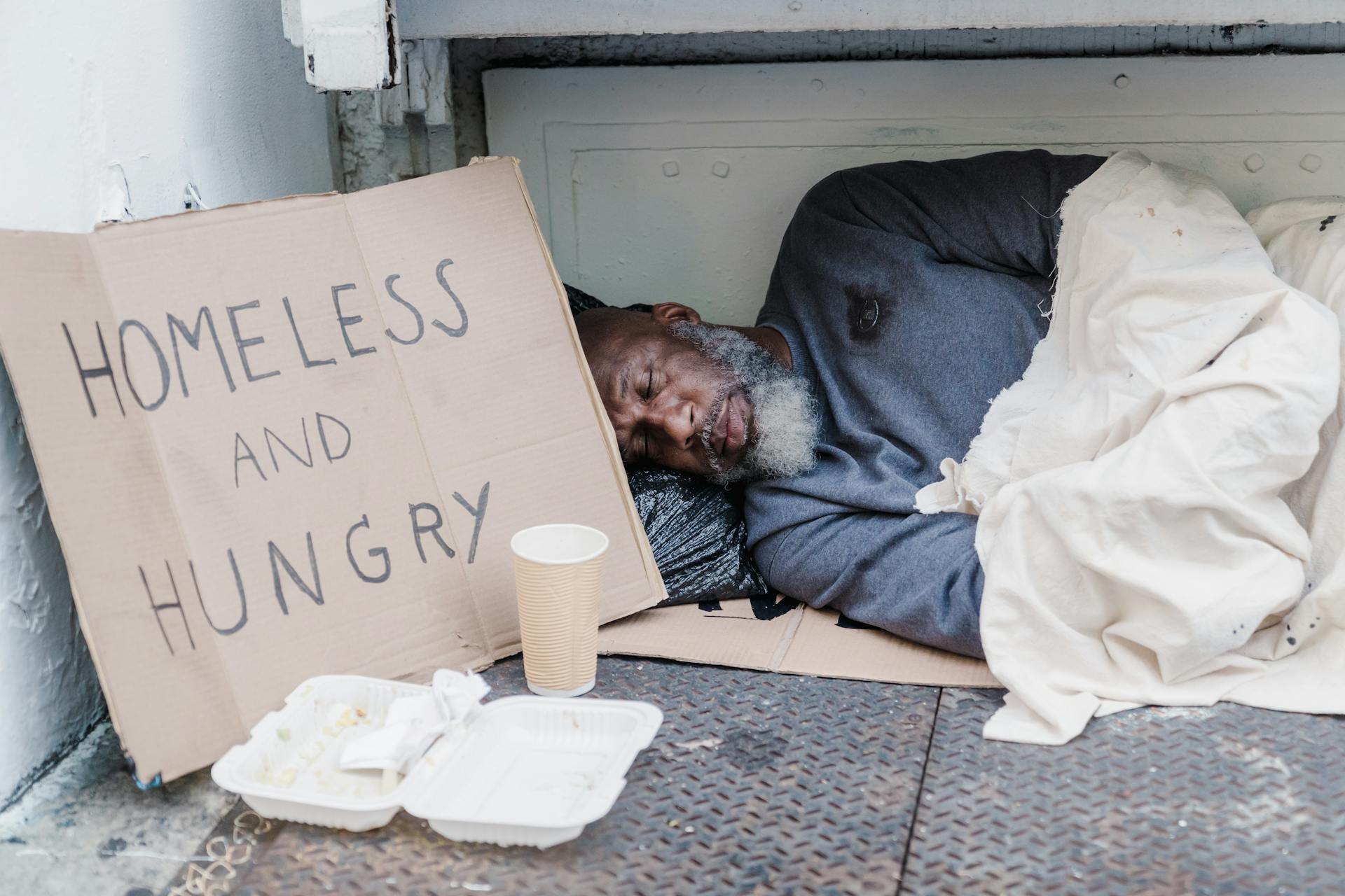 A homeless and hungry man sleeping beside a cardboard sign | Source: Pexels