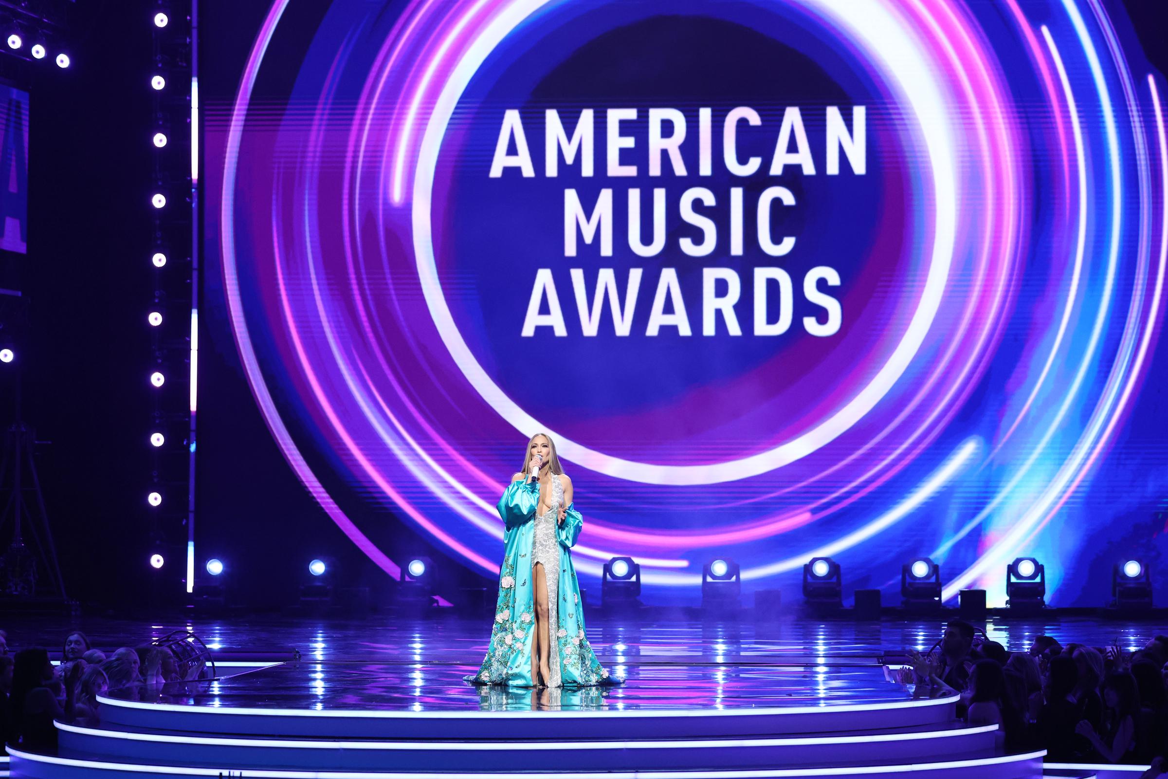 Against a vibrant swirl of pinks and blues, Jennifer Lopez closes her stage moment at the American Music Awards, standing poised beneath the event's towering logo.