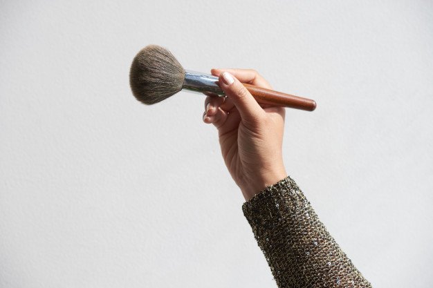 Mano sosteniendo brocha para polvos cosméticos. │Foto: Freepik