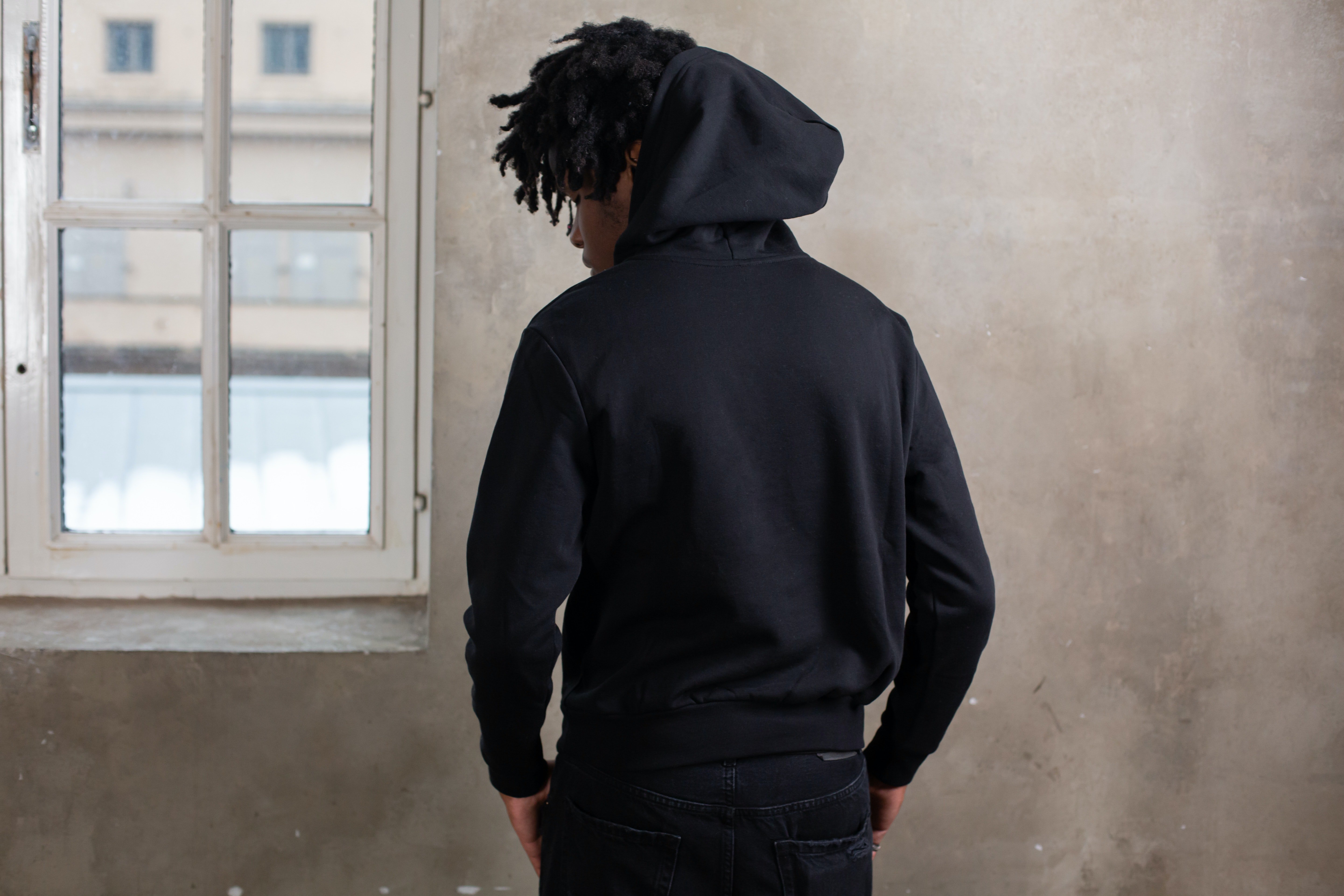 Teenager standing in front of a wall wearing a black hoodie | Photo: Pexels