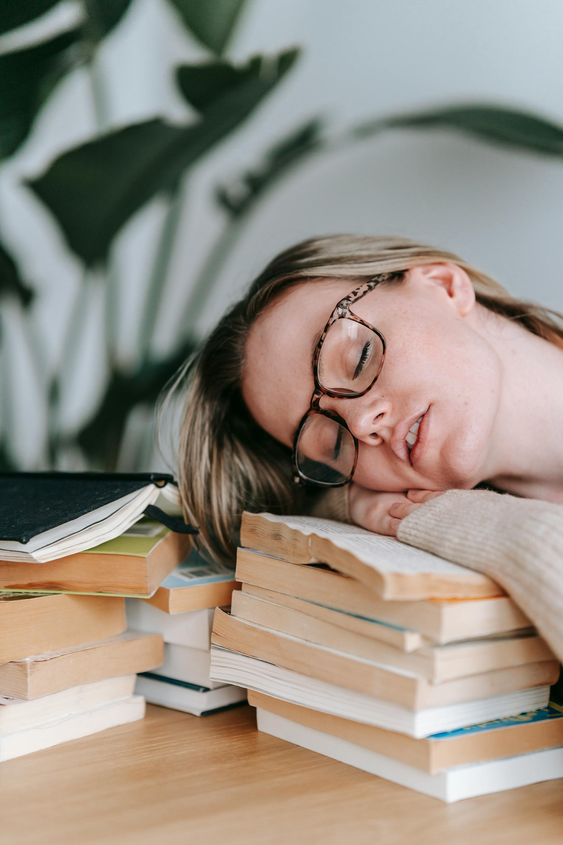 A tired young woman resting her head on a pile of books | Source: Pexels
