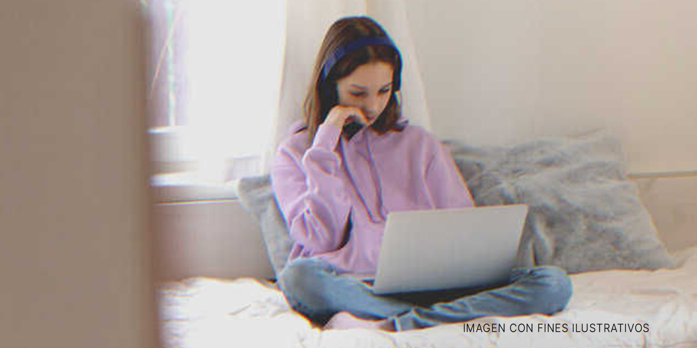 Jovencita sentada sobre la cama con un ordenador. | Foto: Shutterstock