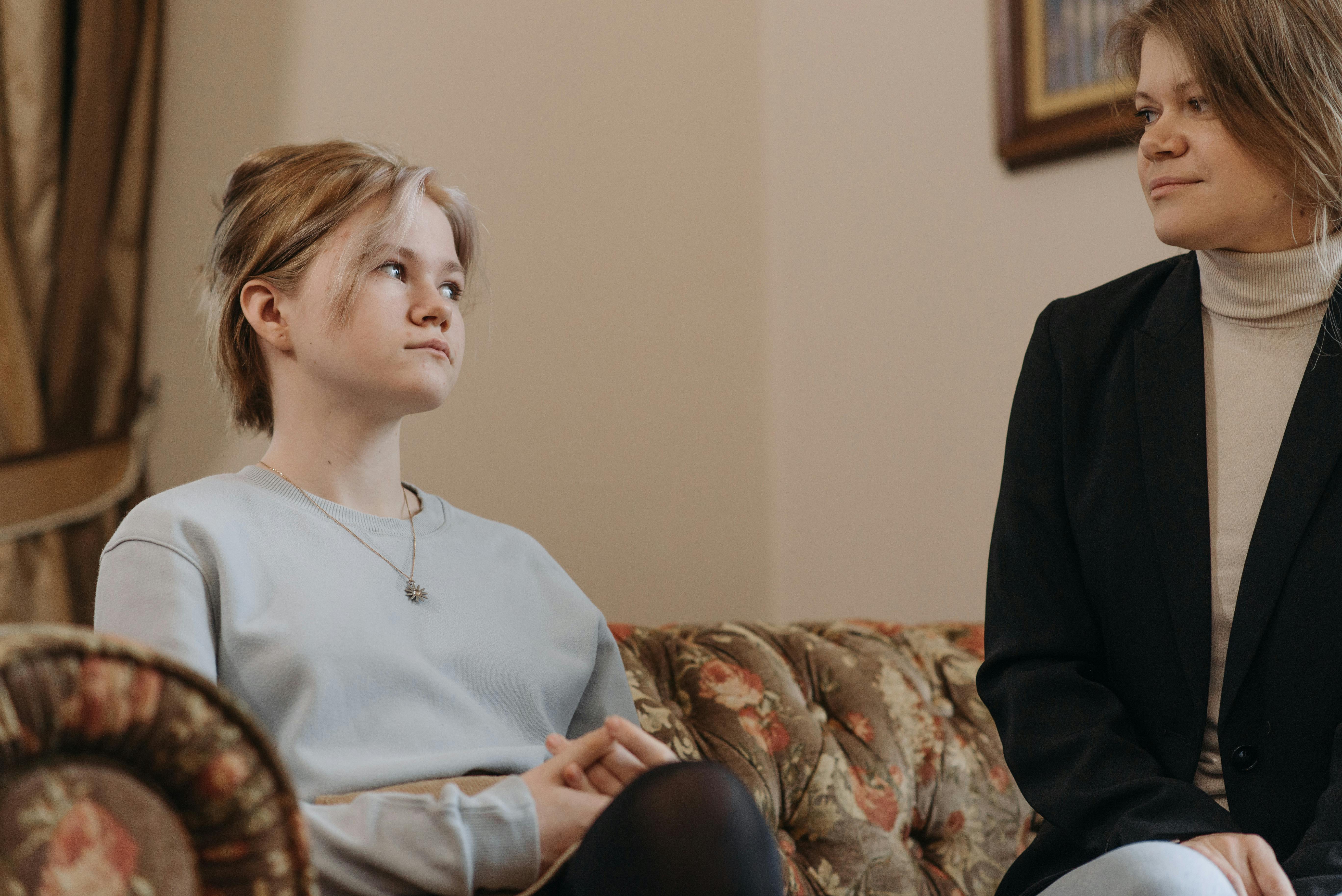 Mother and daughter sitting on a couch while looking at each other | Source: Pexels