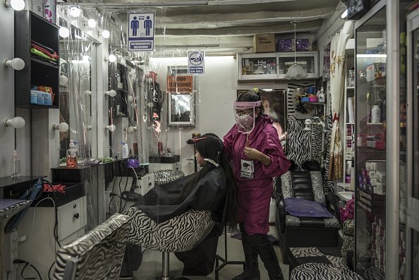 Un styliste portant un masque de protection et un bouclier coupe les cheveux d'une cliente.|Photo : Getty Images