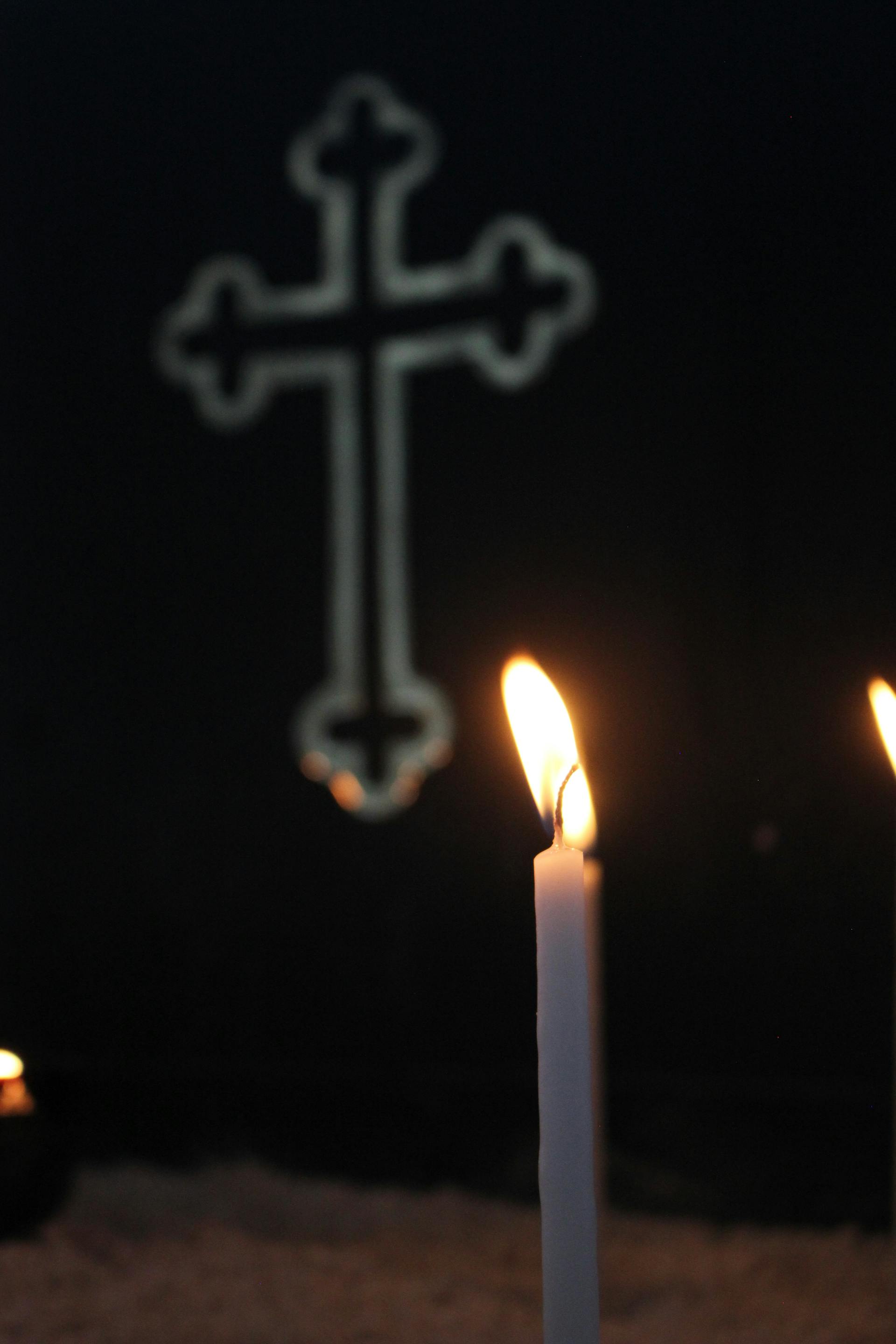 A burning wax candle against the backdrop of a cross | Source: Pexels