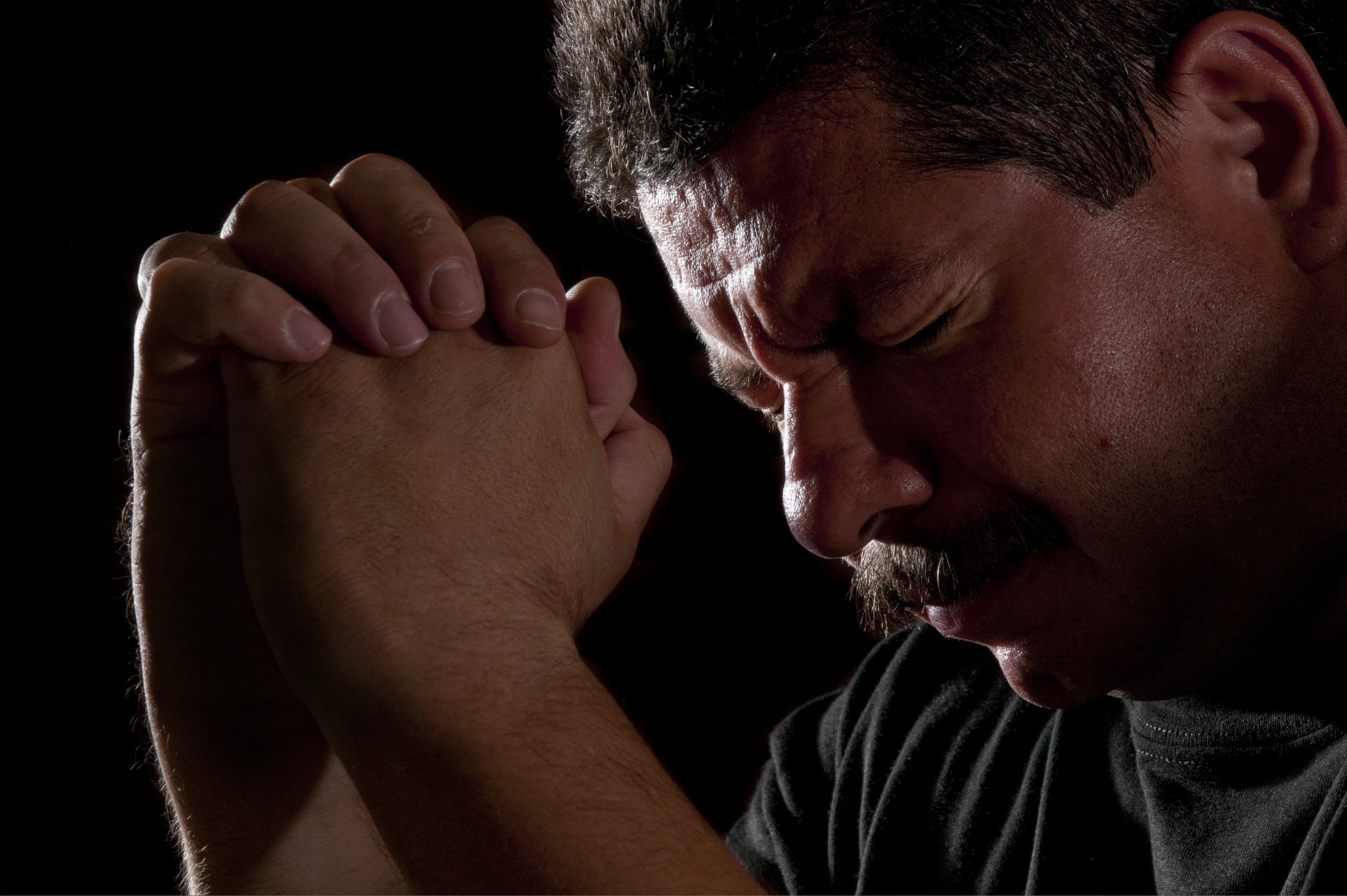 Man praying with head bowed in the dark. | Photo: Getty Images