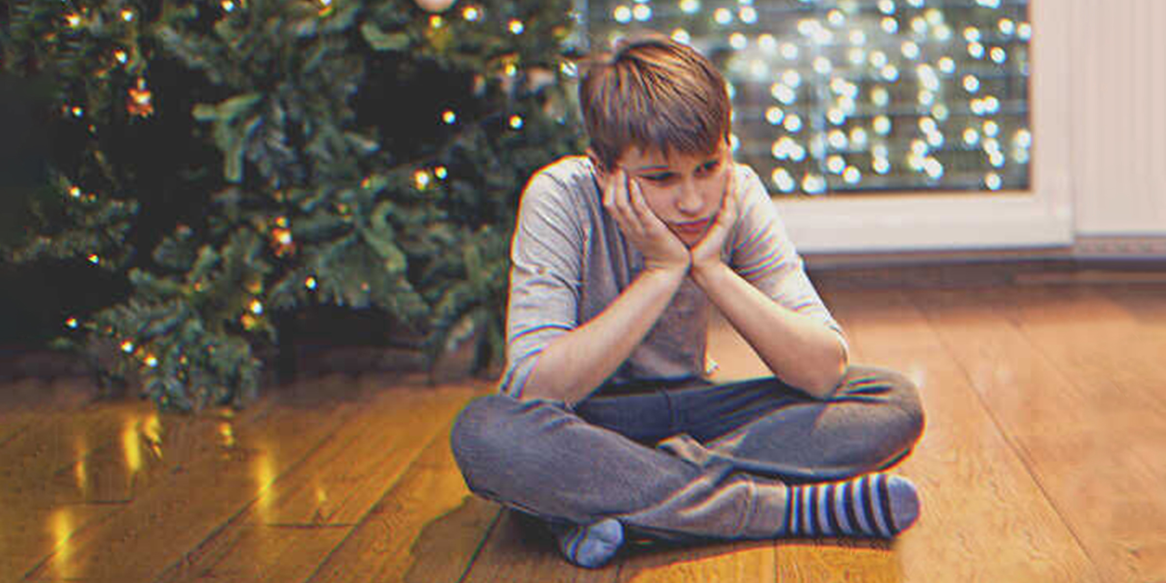 Ein Junge sitzt auf dem Boden neben einem Weihnachtsbaum. | Quelle: Getty Images
