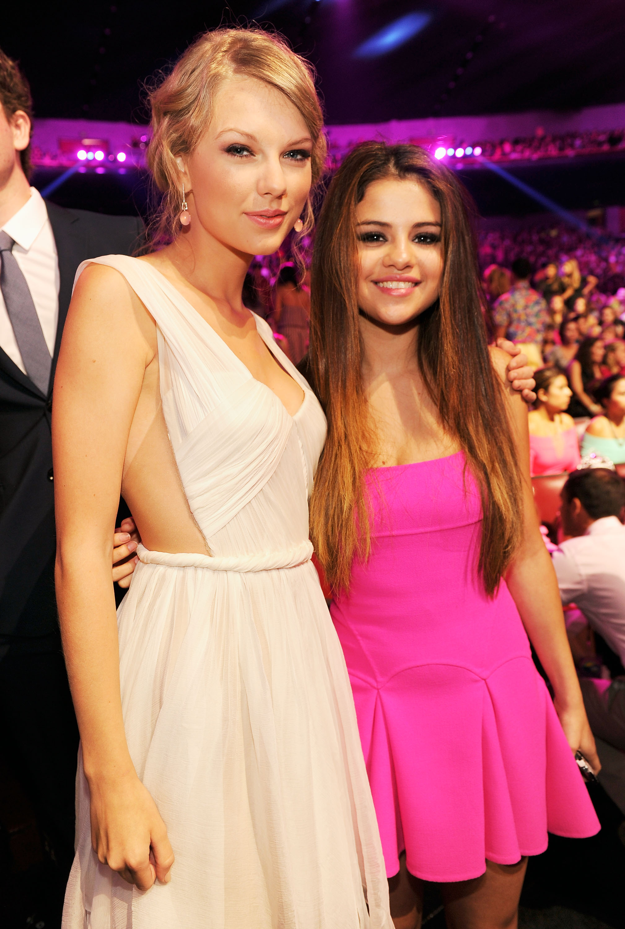 At the Teen Choice Awards, Taylor Swift and Selena Gomez share smiles inside the venue, donning elegant white and bold pink looks that capture their youthful energies.
