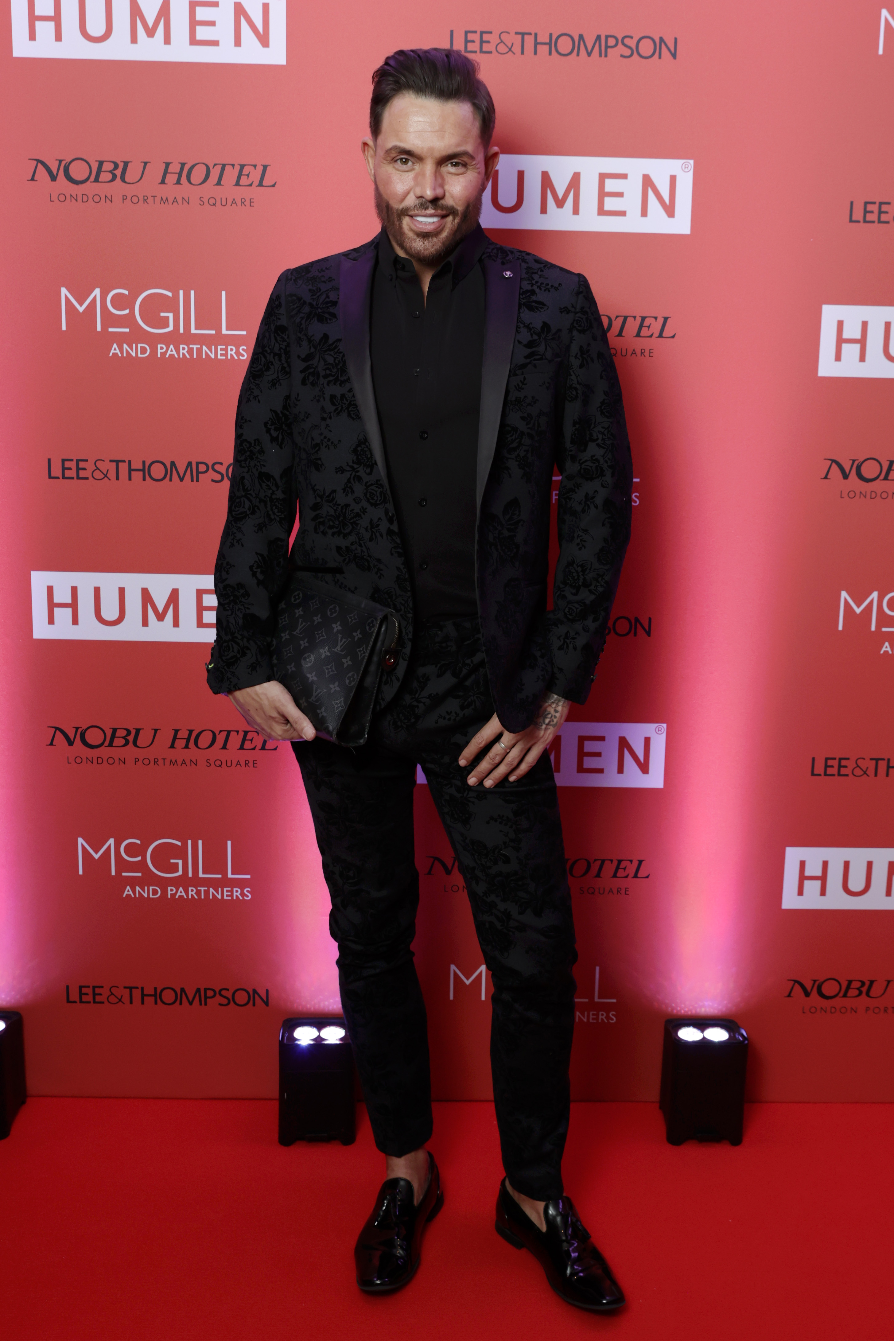 At the HUMEN Orange Ball at Nobu London in October 2024, Norris cut a sleek figure in a black floral jacquard suit with satin lapels and patent loafers, his beard neatly trimmed and his face noticeably more defined following the removal of his fillers.
