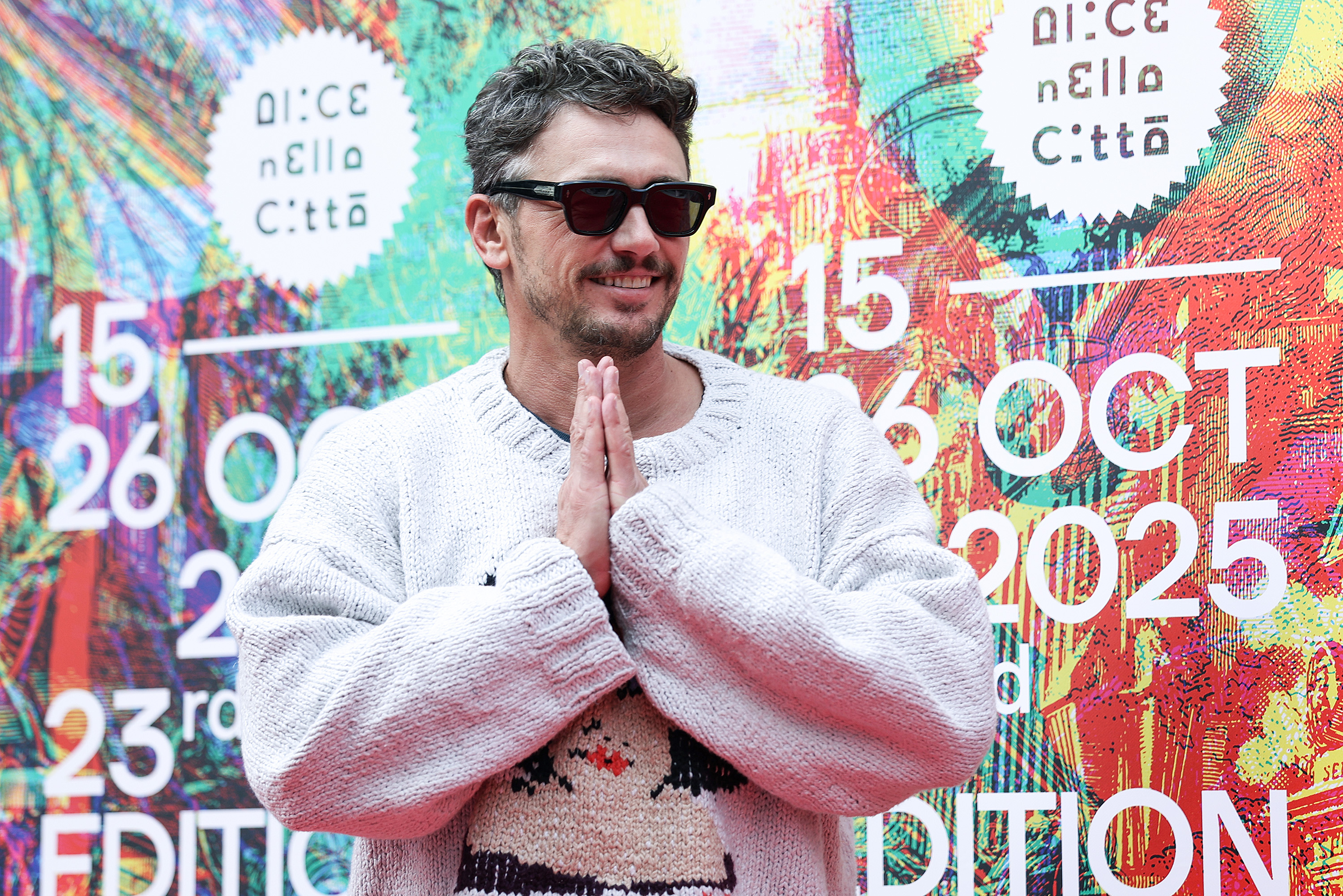 During the "Squali" photocall, James Franco greets attendees with a prayer-like gesture and a grin, showing a lighter, more playful side amid press interactions in Rome.