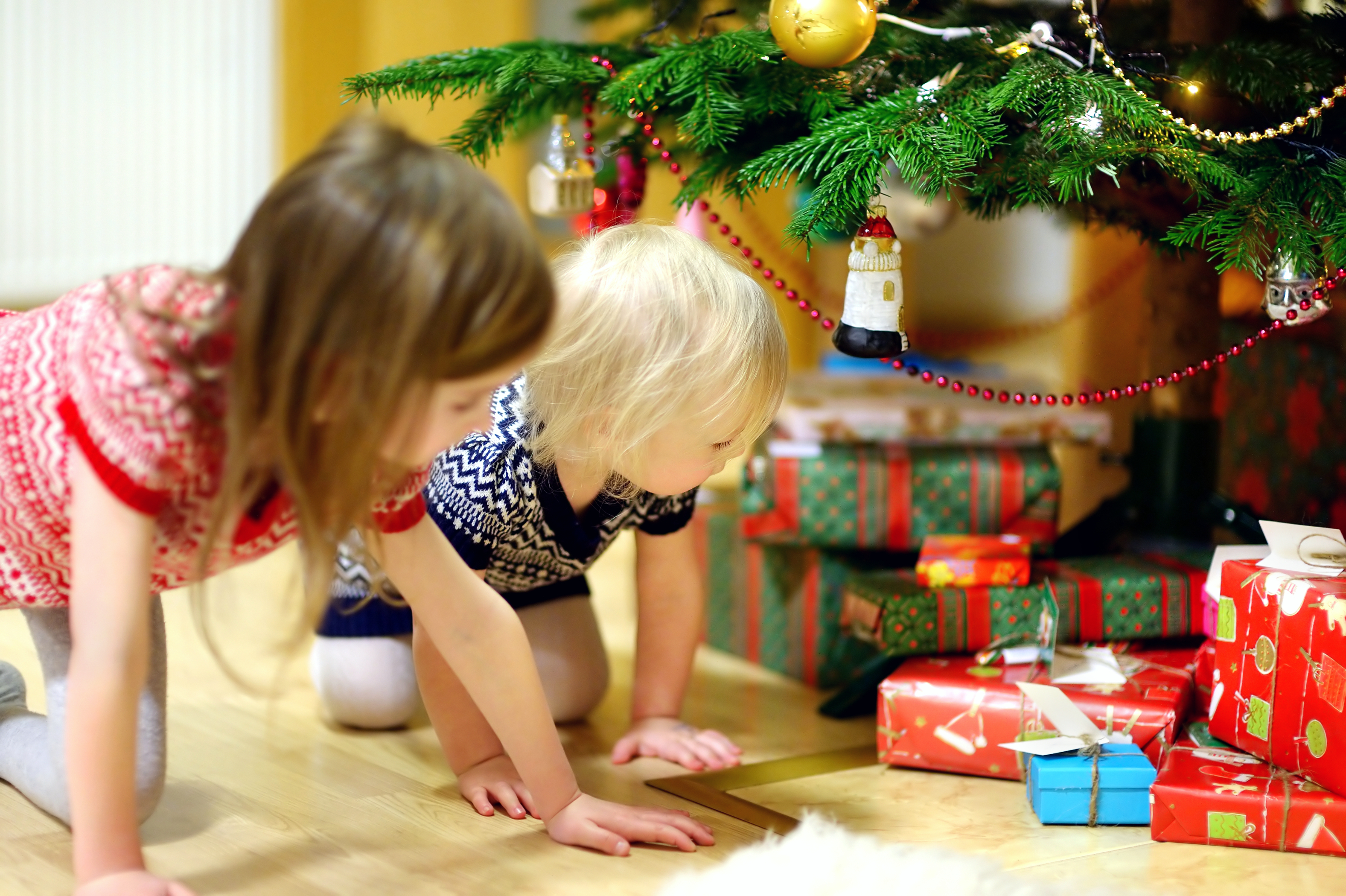 Two little sisters looking for gifts under a Christmas tree | Source: Shutterstock