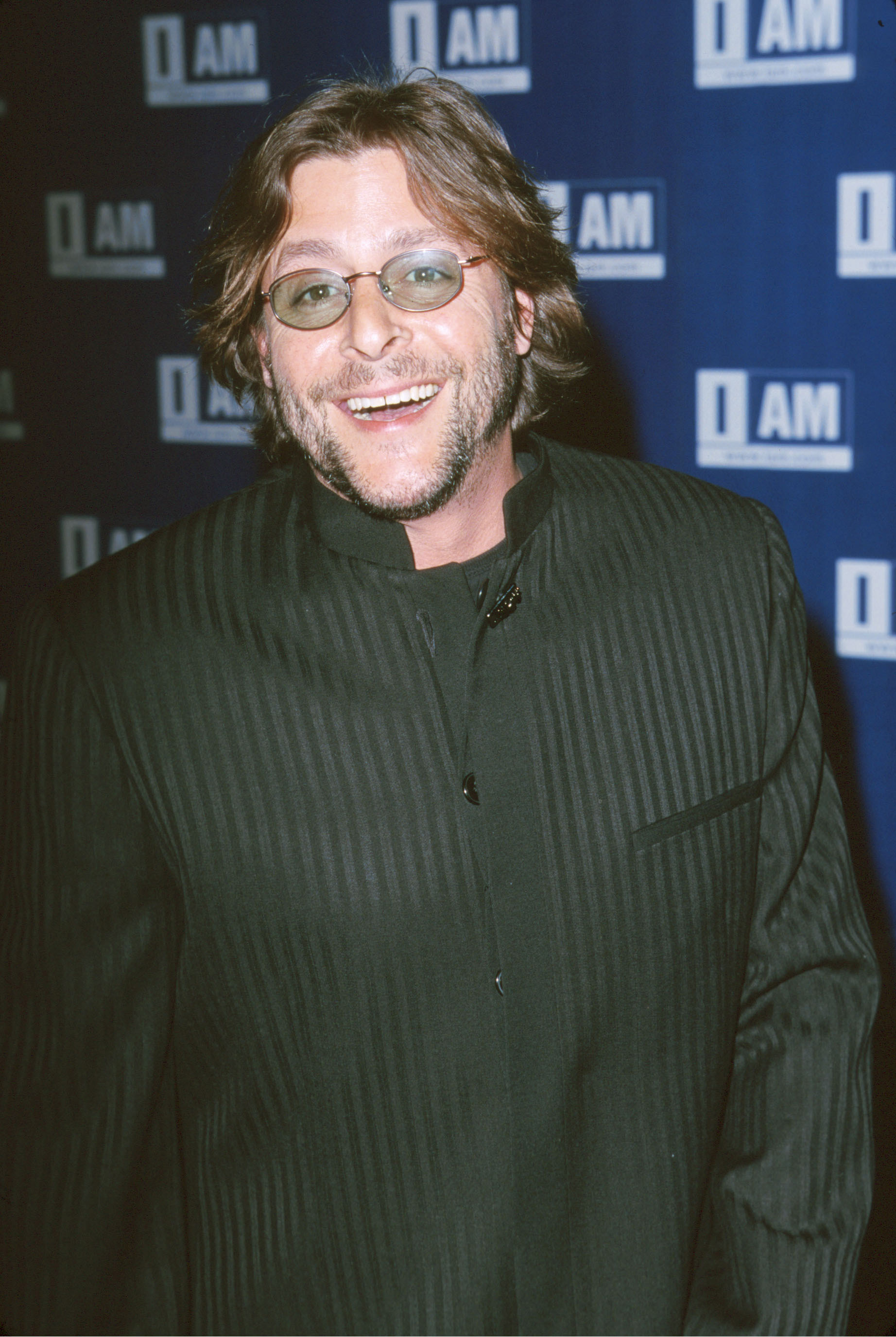 Sporting tinted oval glasses, facial stubble, and a dark pinstriped mandarin-collar jacket, the actor smiled brightly on the red carpet during the IAM.com Hollywood Launch Party at Quixote Studios in Hollywood on March 21, 2000. | Source: Getty Images