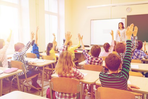 A classroom with students who have their hands raised to answer a question. | Source: Shutterstock.