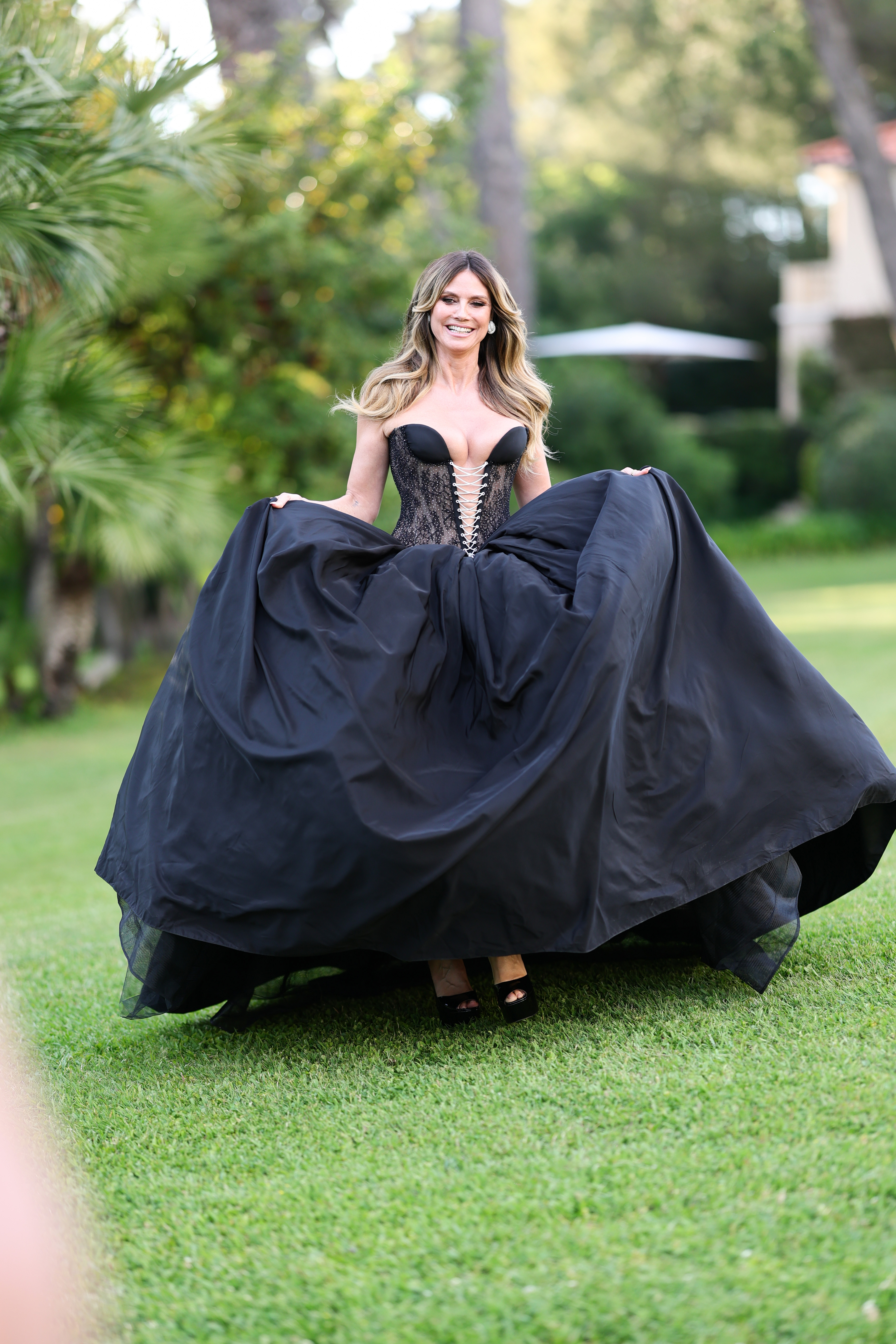 Heidi Klum stands on a grassy lawn surrounded by trees as the dramatic skirt of her gown spreads around her. | Source: Getty Images