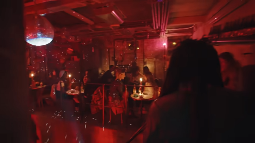 The basement club, bathed in a moody red glow, features small candlelit tables where guests can lounge beneath a glittering disco ball. | Source: YouTube/@Archdigest