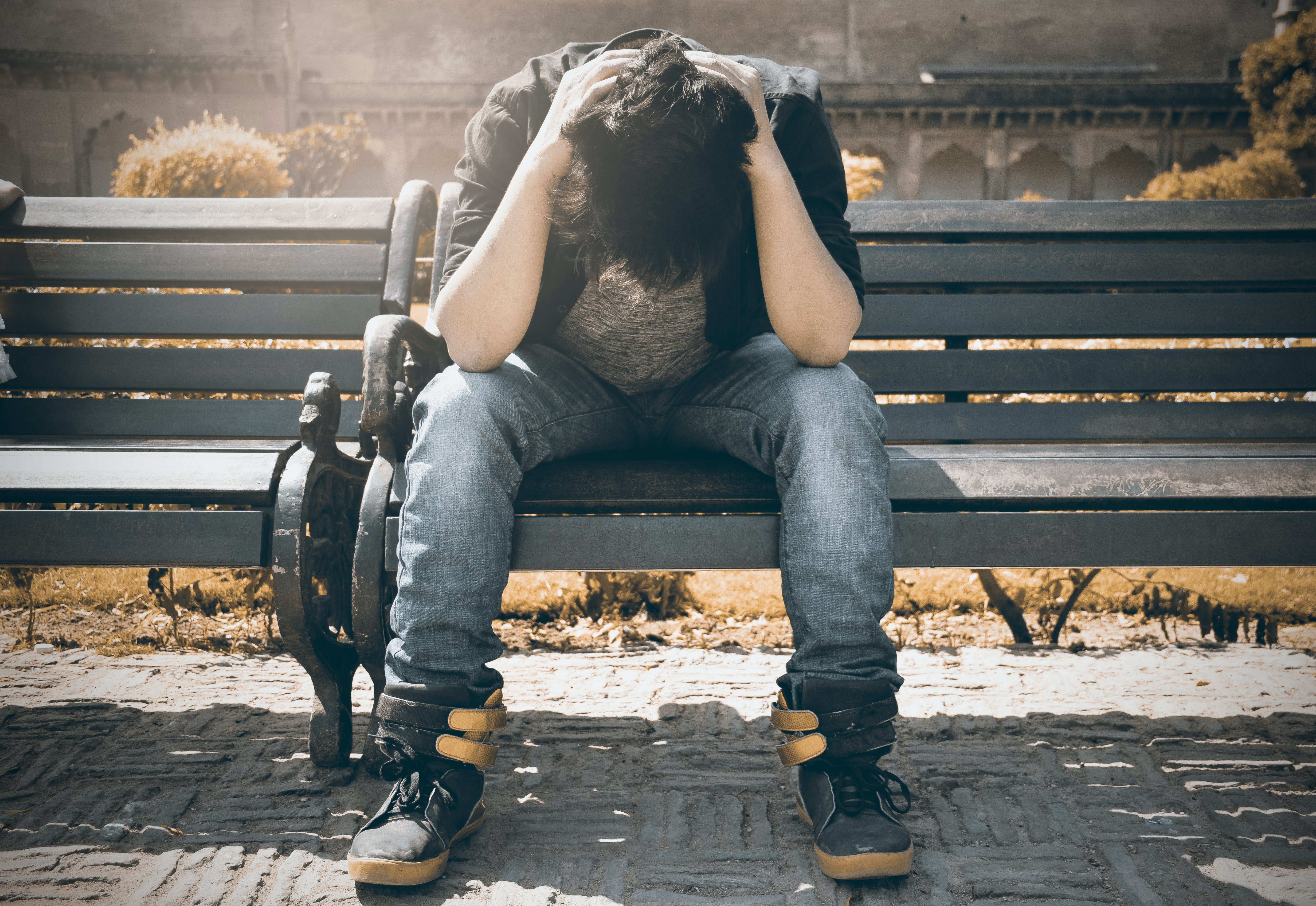 An upset man sitting on a bench facing down with his hands over his head | Source: Pexels