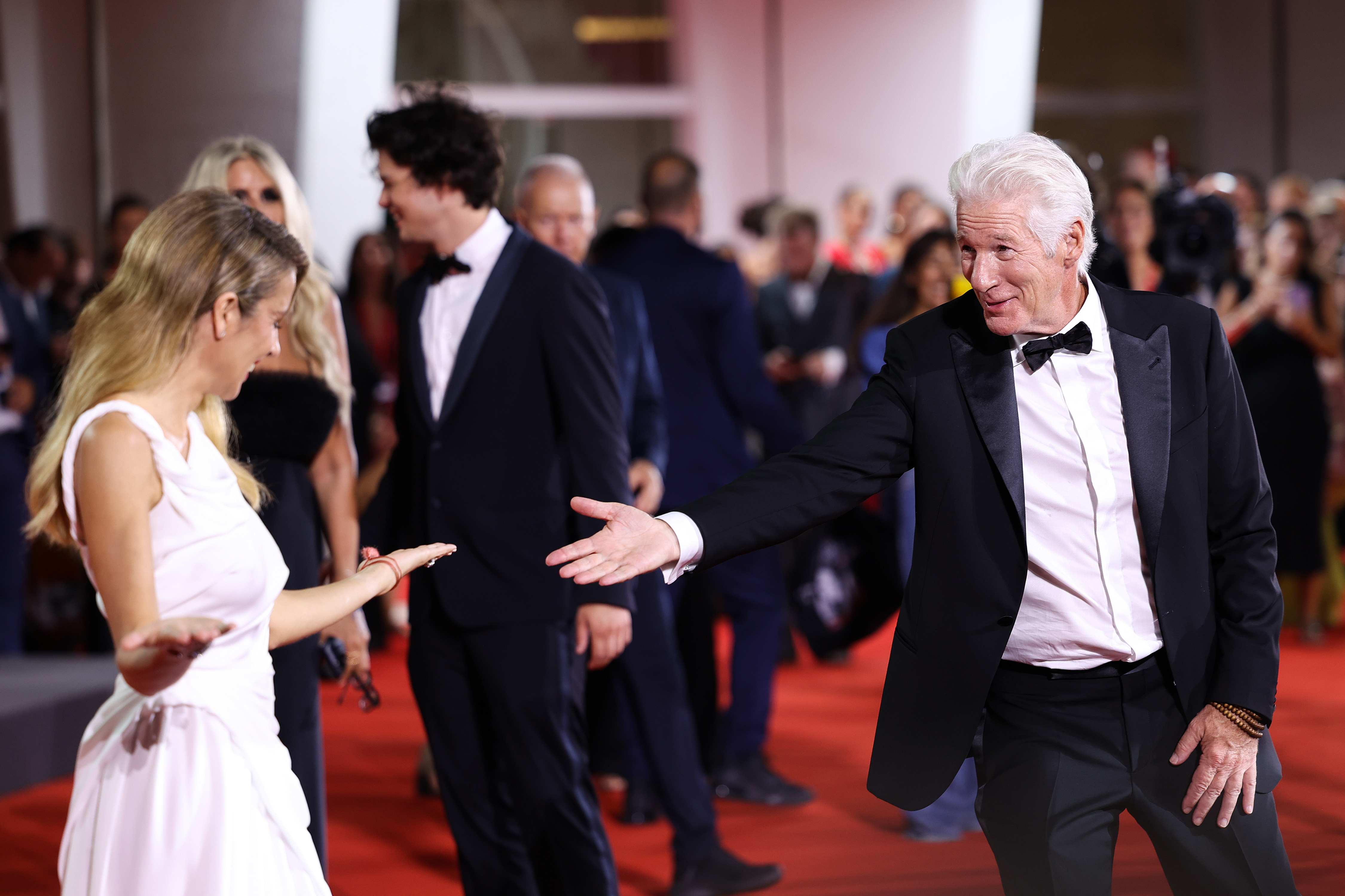 Richard Gere reaches toward Alejandra Silva in a playful exchange during the Filming Italy Venice Award red carpet at the 81st Venice International Film Festival, held September 1, 2024, in Venice, Italy.