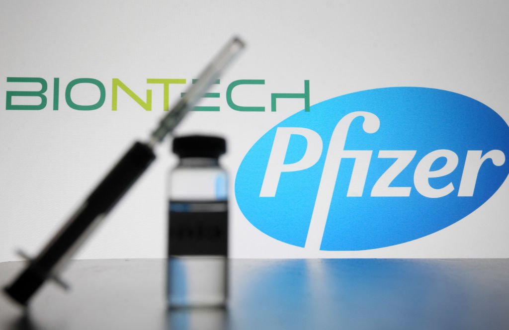 Eine Spritze und eine kleine Flasche vor dem amerikanischen multinationalen Pharmaunternehmen Pfizer und dem deutschen Biotechnologieunternehmen Biontech Logos. | Quelle: Getty Images