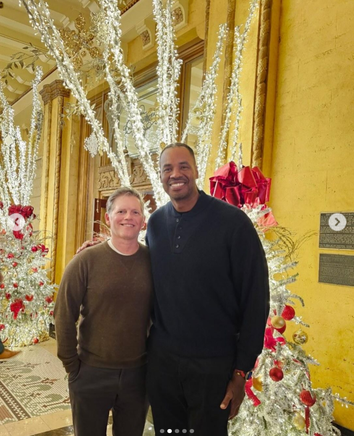 Jason Collins smiles beside his husband, Brunson Green, as the couple pose together in front of sparkling Christmas decorations and illuminated white trees during the holiday season. | Source: Instagram/jasoncollins_98