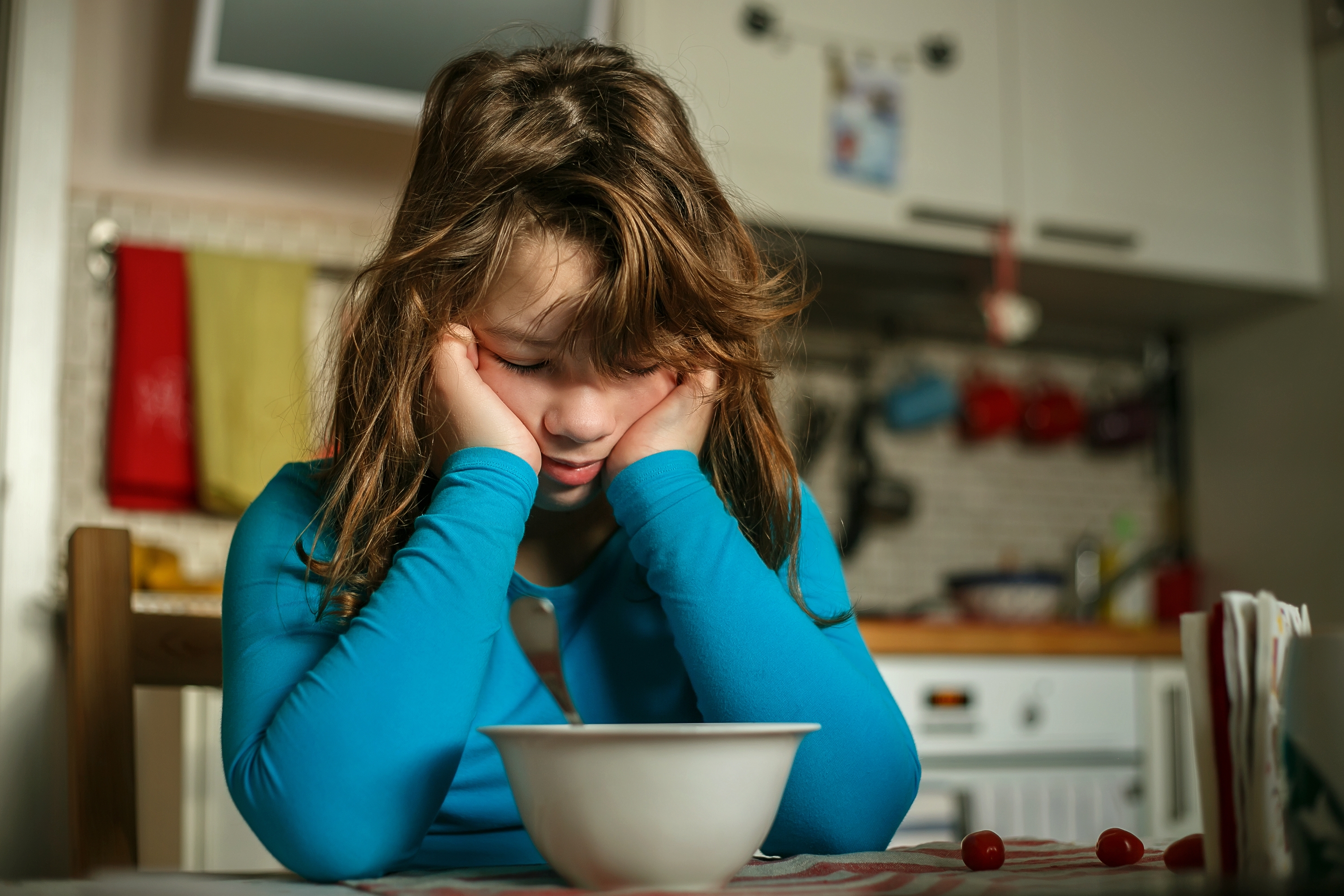 The girl bent over her breakfast plate in a disgruntled pose | Source: Shutterstock.com