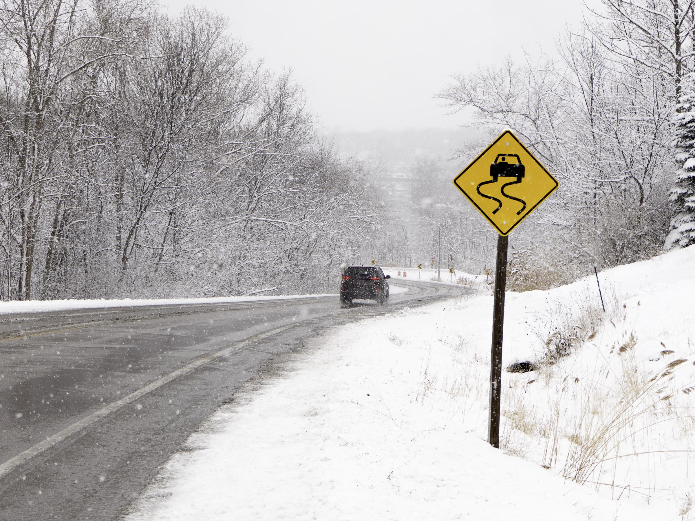 An icy downhill road with a "Slippery When Wet" sign, dated March 21, 2018 | Source: Getty Images